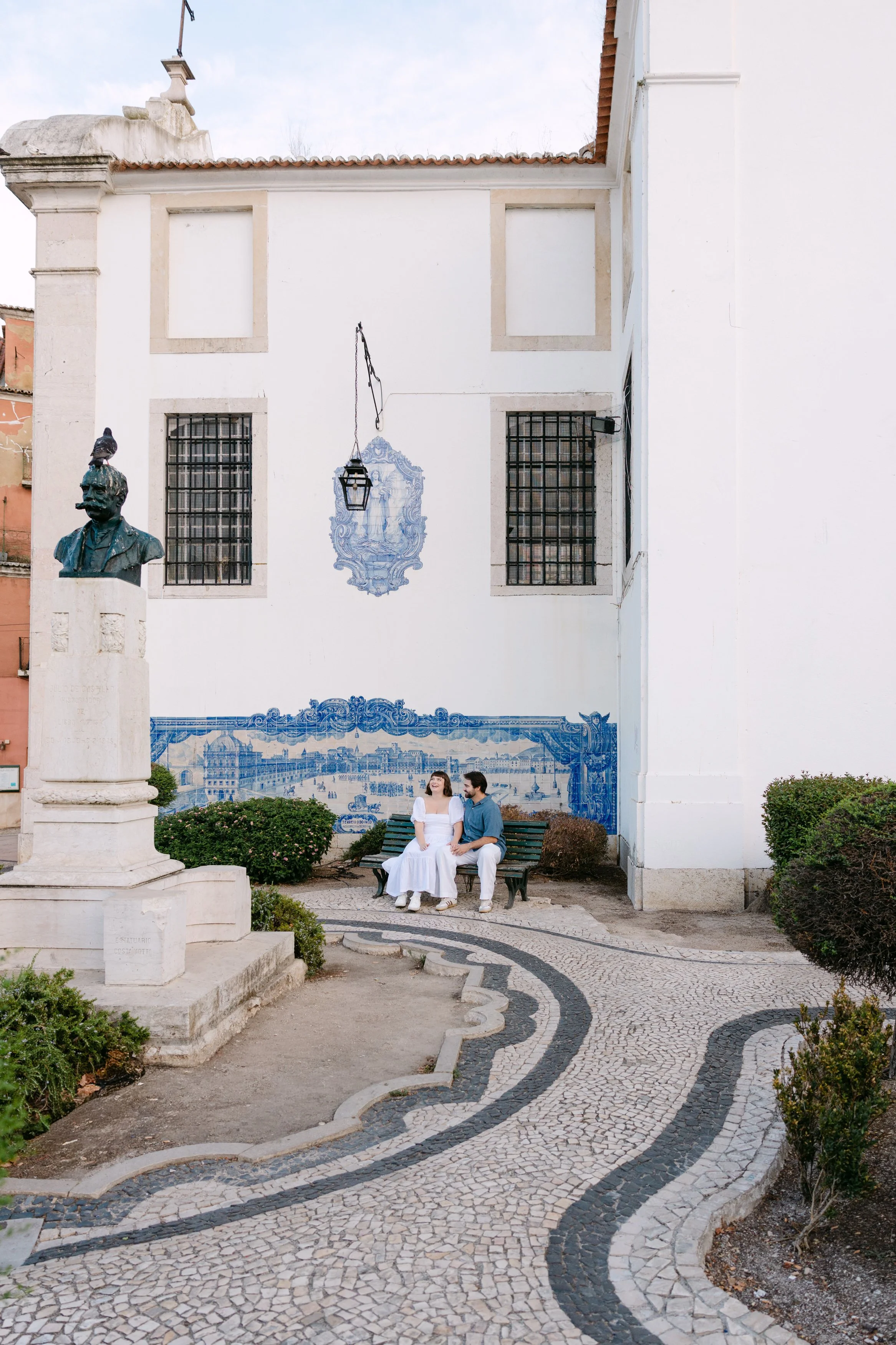 Newly engaged couple sitting together beside the blue tiled walls of Miradouro de Santa Luzia in Lisbon.