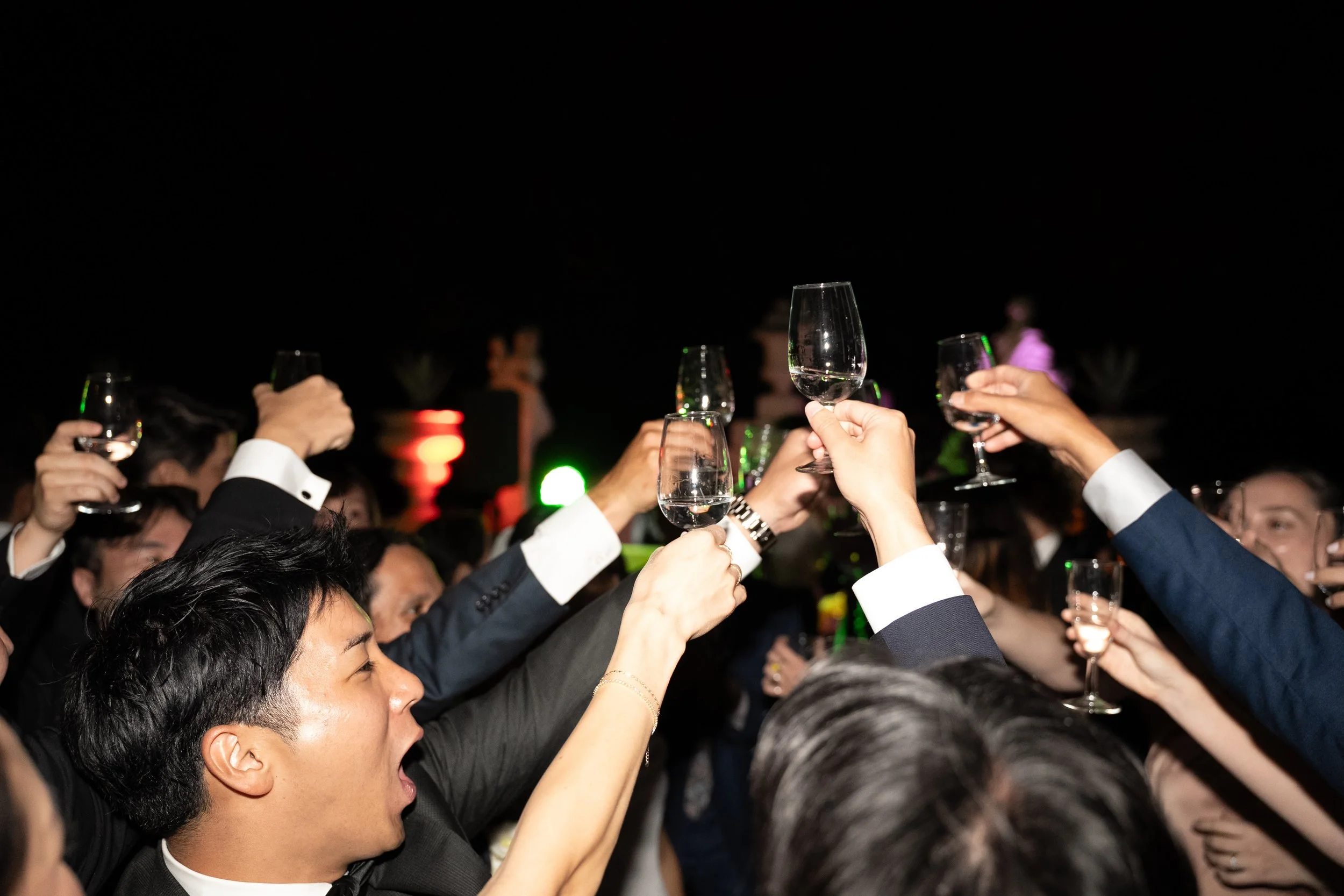 Wedding guests raising their glasses together during a lively nighttime wedding party at Palácio Nacional de Queluz.
