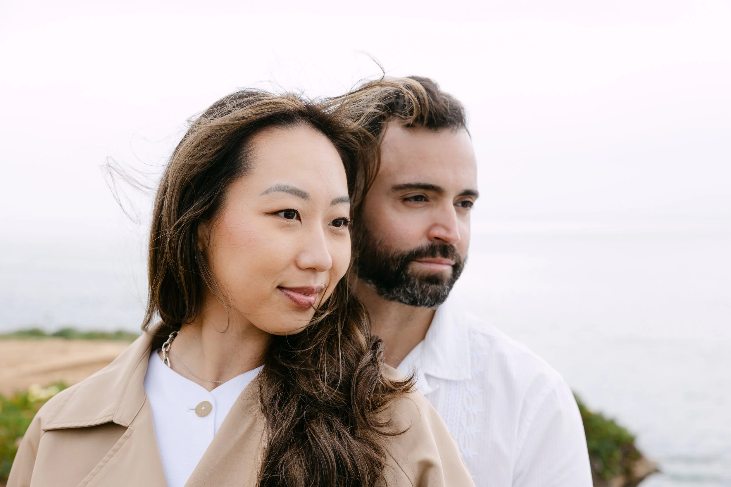 Romantic windswept portrait of engaged couple during coastal engagement session in Portugal.