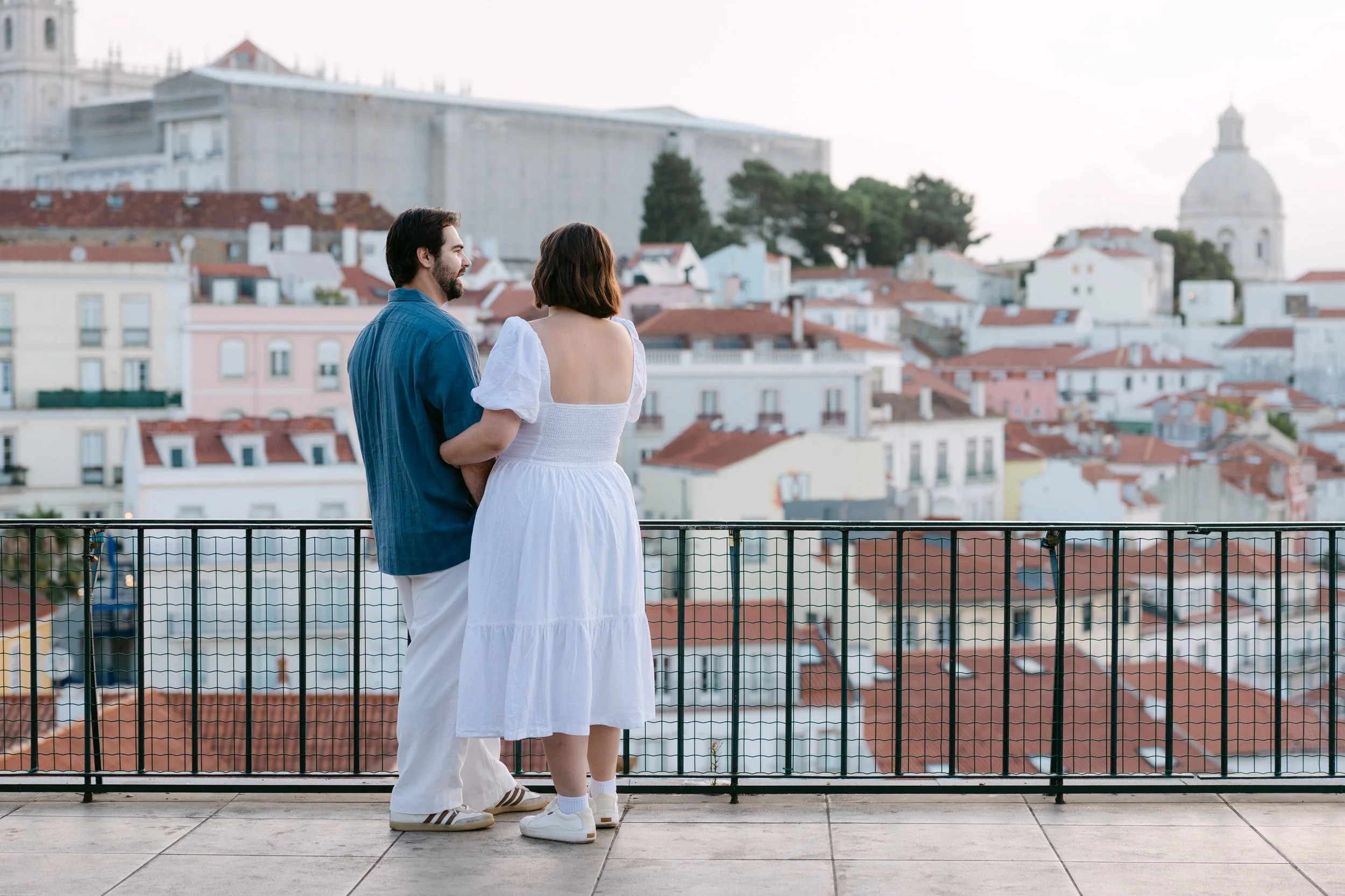 Newly engaged couple looking over the rooftops of Alfama from Miradouro das Portas do Sol in Lisbon.