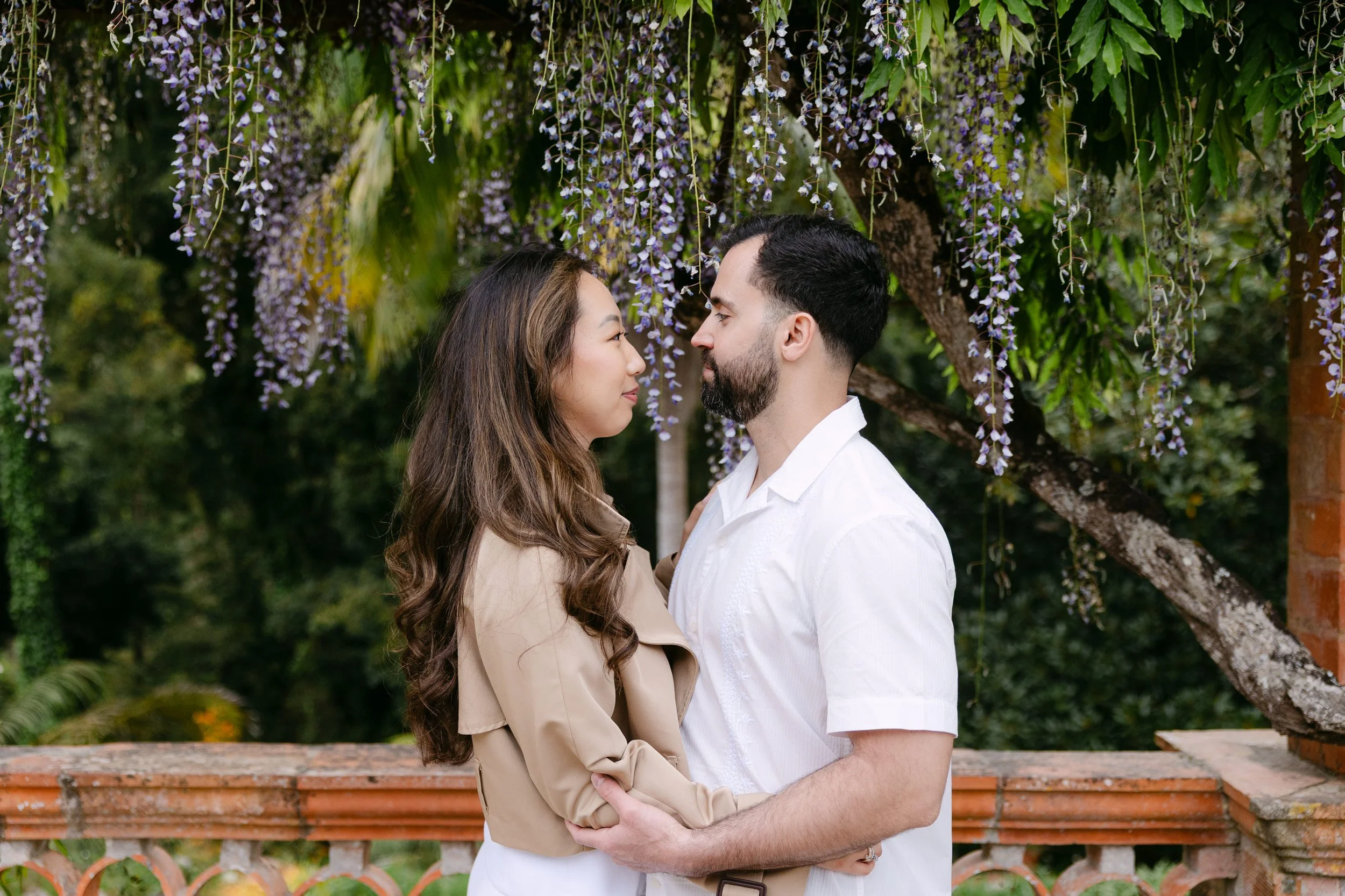 Romantic couple portrait under hanging purple wisteria flowers at Monserrate Palace gardens.