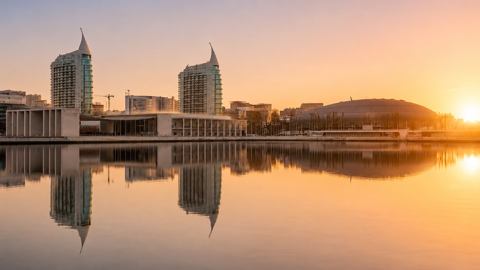 Sunrise over Parque das Nações in Lisbon with reflections of modern architecture and waterfront buildings.