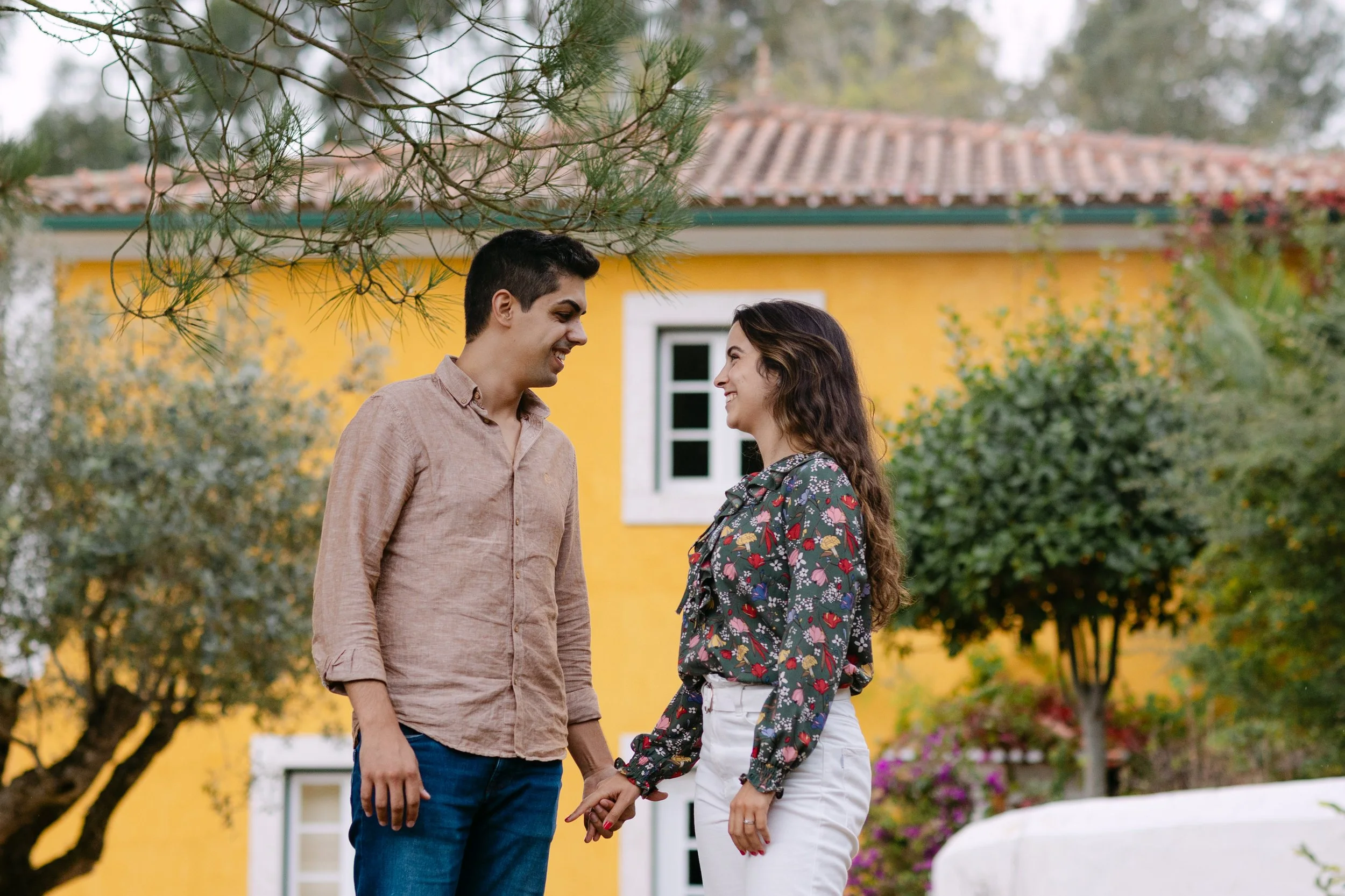 Recently engaged couple smiling at each other outside yellow house at Quinta de Santana