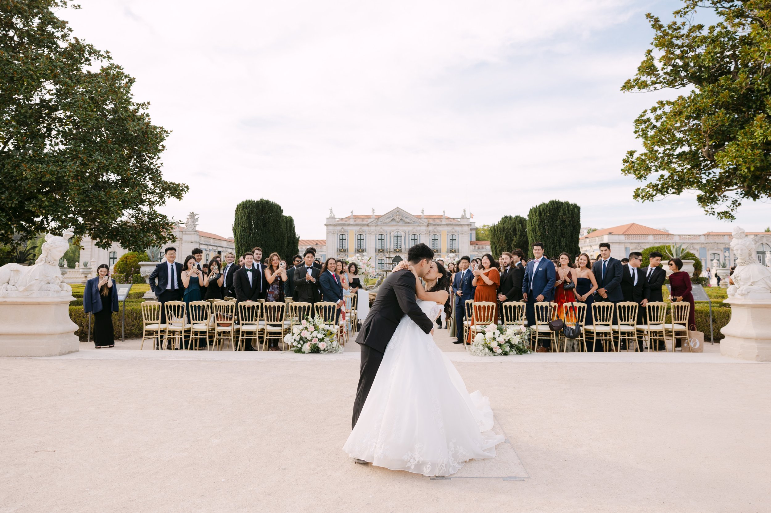 Newlyweds kissing in front of their cheering wedding guests after their outdoor ceremony in the gardens of Palácio Nacional de Queluz.