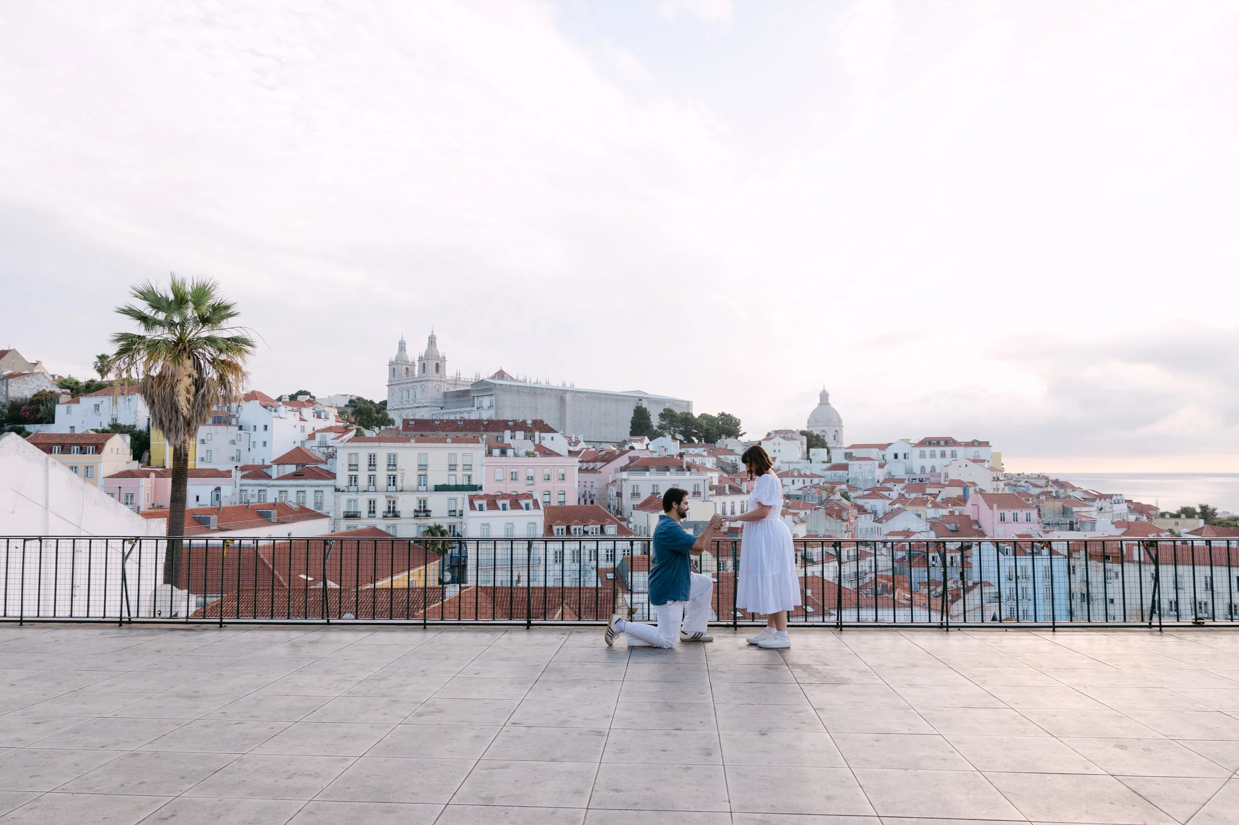 Emily reacting as Abraham proposes during their sunrise proposal at Miradouro das Portas do Sol in Lisbon.