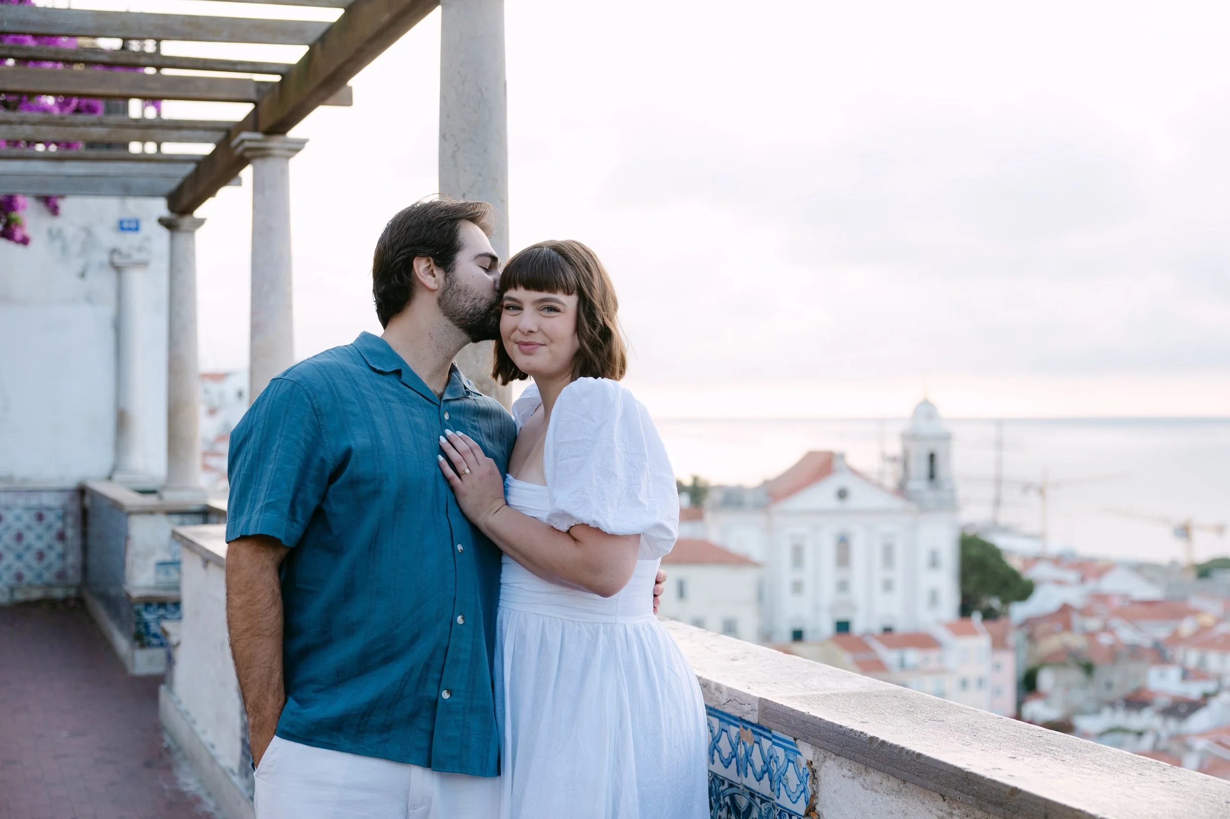 Couple embracing at Miradouro de Santa Luzia with Alfama and the Tagus River behind them after their Lisbon proposal.