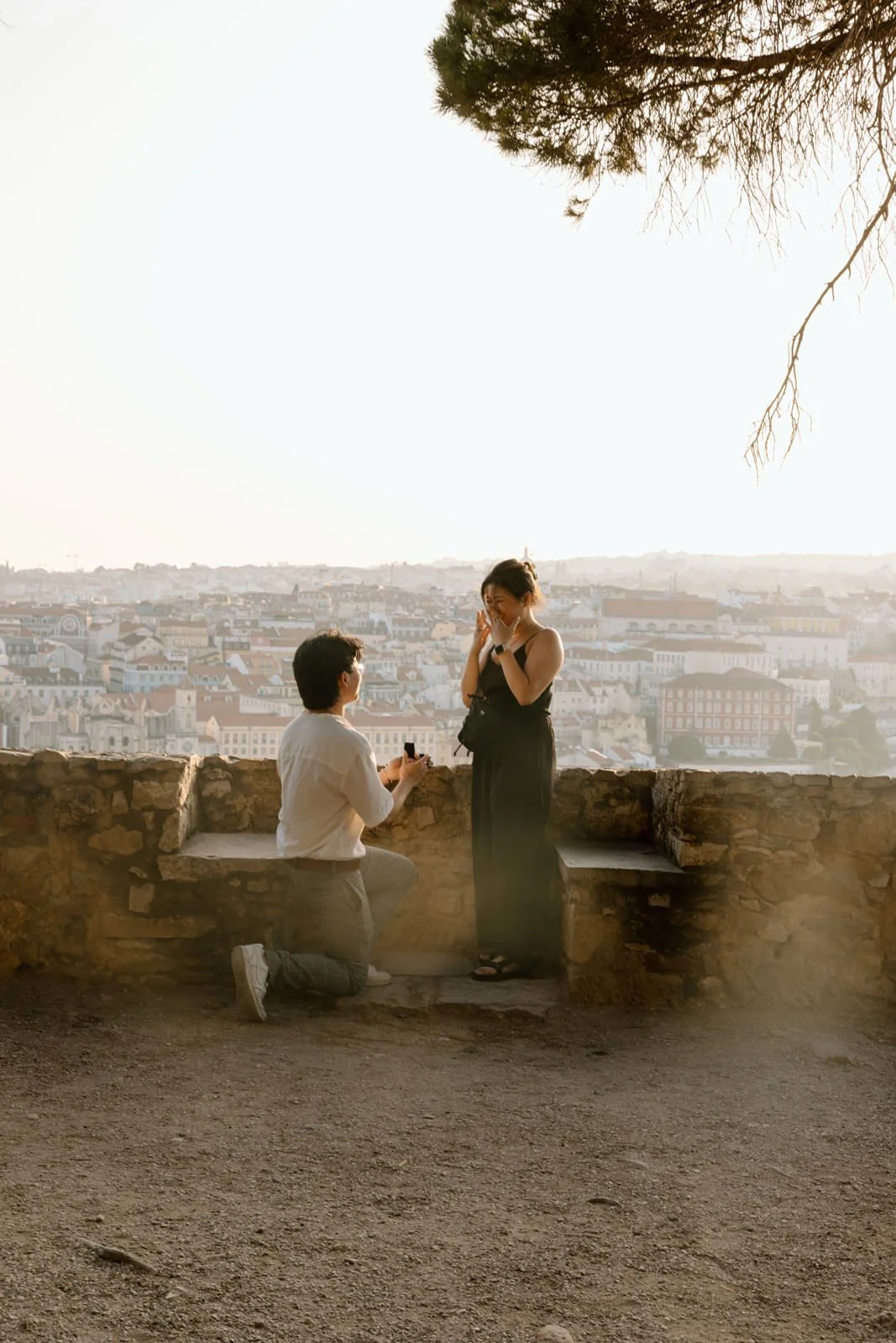 Couple during a surprise proposal at Castelo de São Jorge overlooking Lisbon at sunset.
