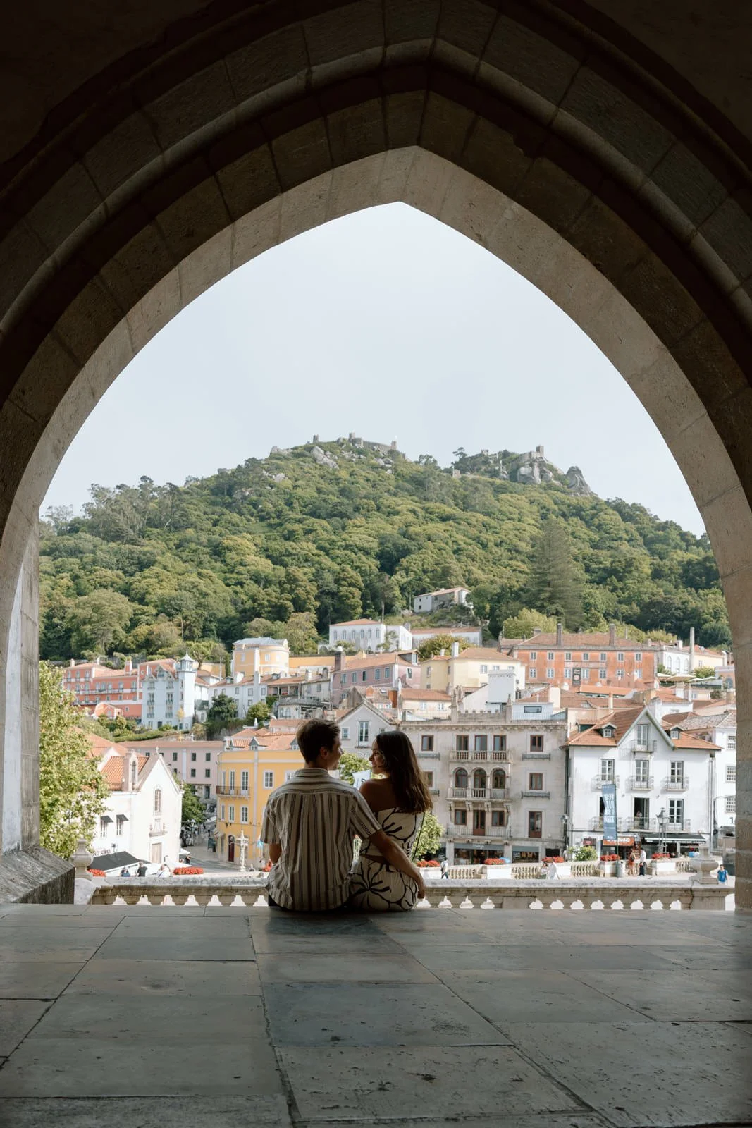 Recently engaged couple sitting beneath the historic arches of Palácio Nacional de Sintra with views across Sintra Village.