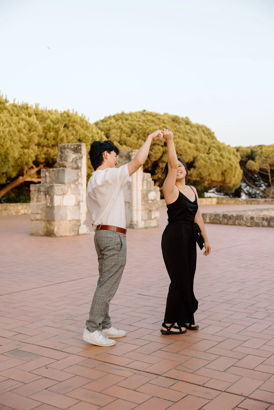 Couple celebrating their engagement with a playful dance during a sunset photo session at Castelo de São Jorge in Lisbon.