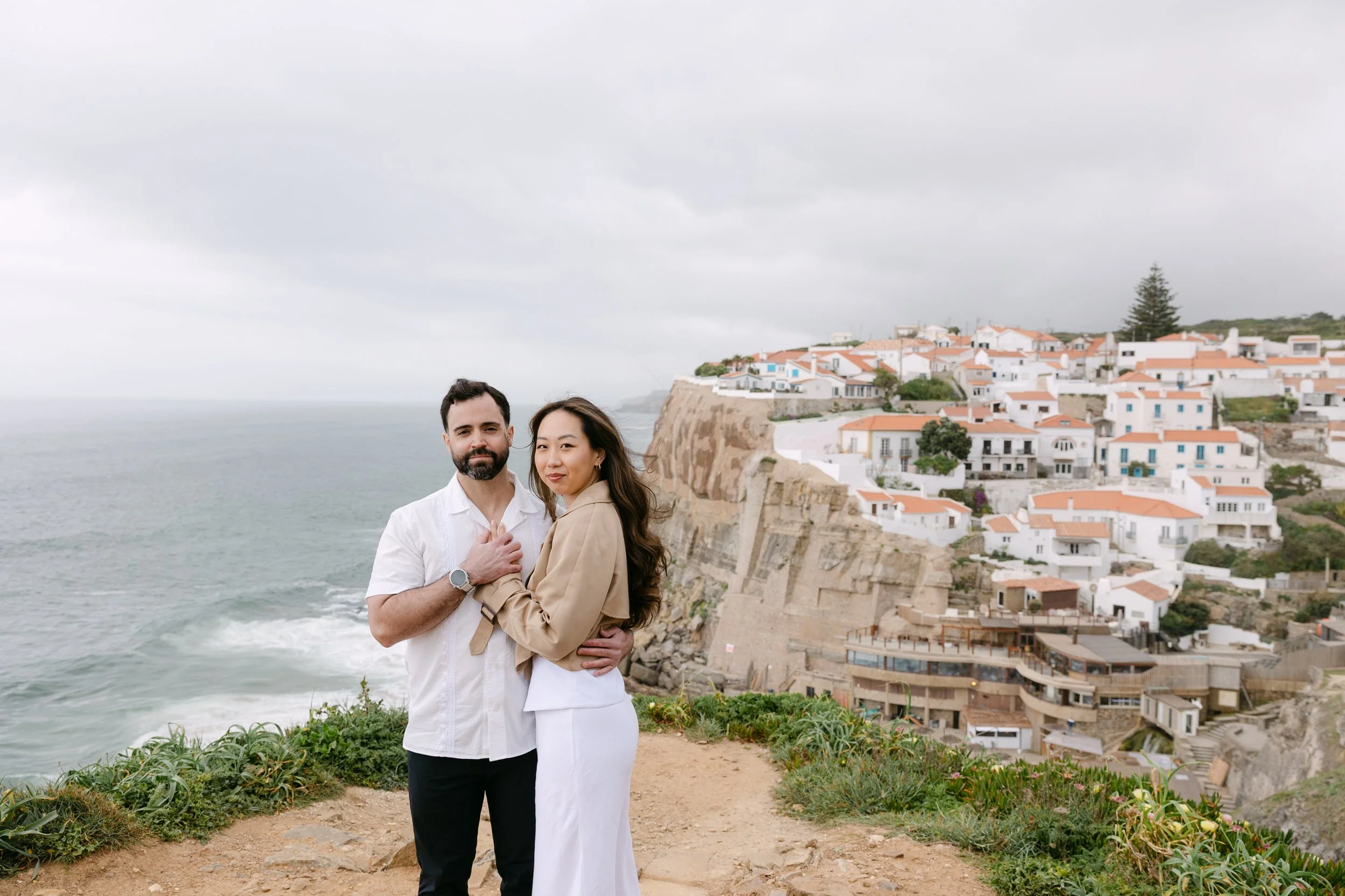 Engaged couple embracing with ocean views over Azenhas do Mar in Sintra, Portugal.