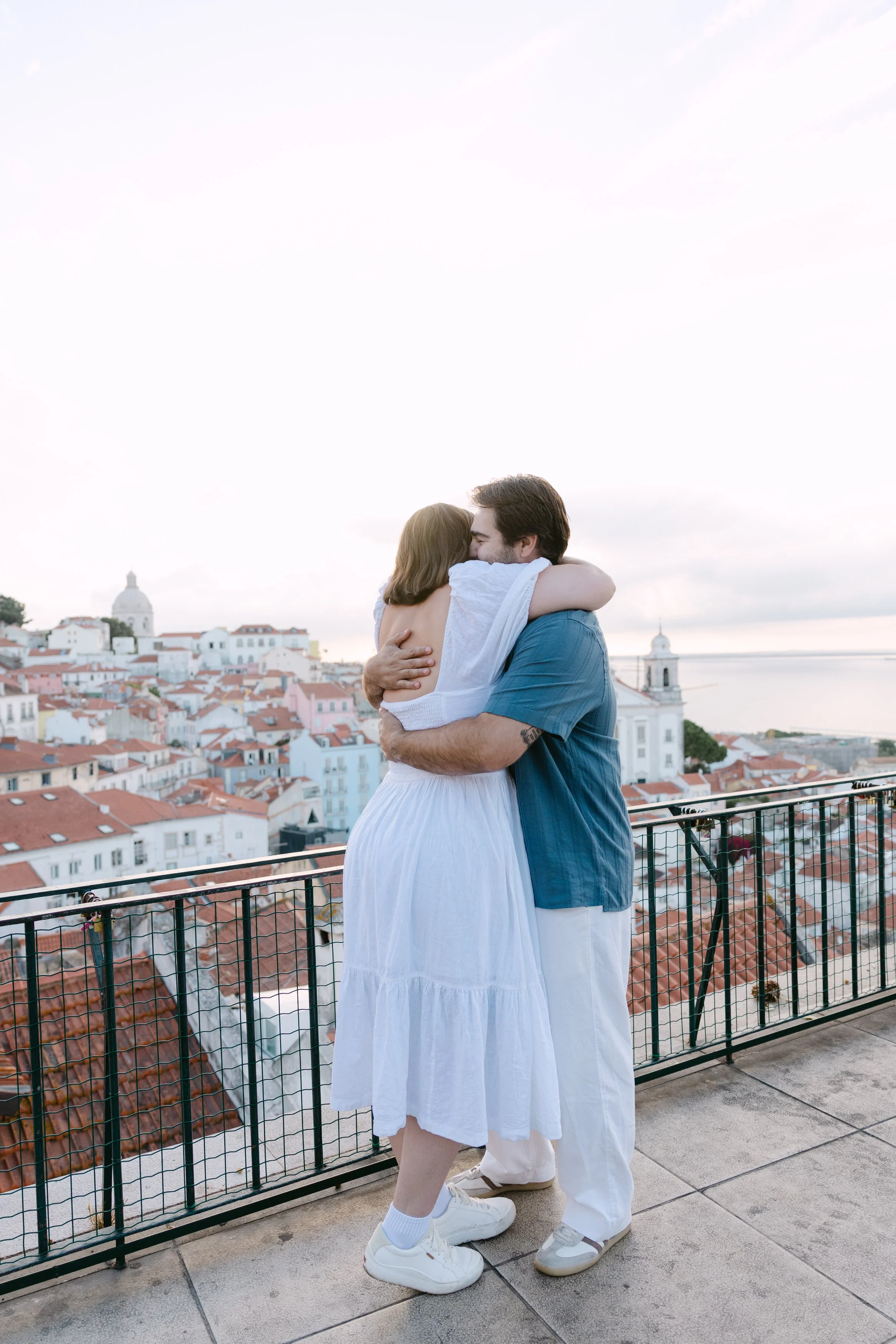Newly engaged couple embracing at Portas do Sol overlooking the rooftops of Alfama in Lisbon.