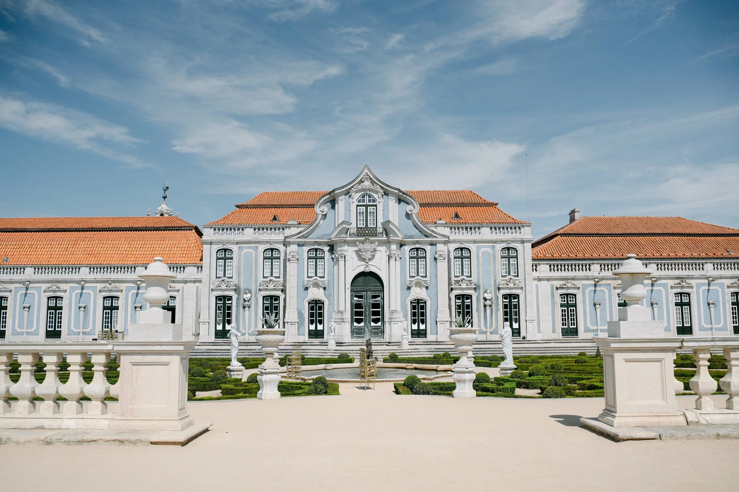 Grand blue and white façade of Palácio Nacional de Queluz overlooking its formal gardens on a sunny wedding day in Portugal.