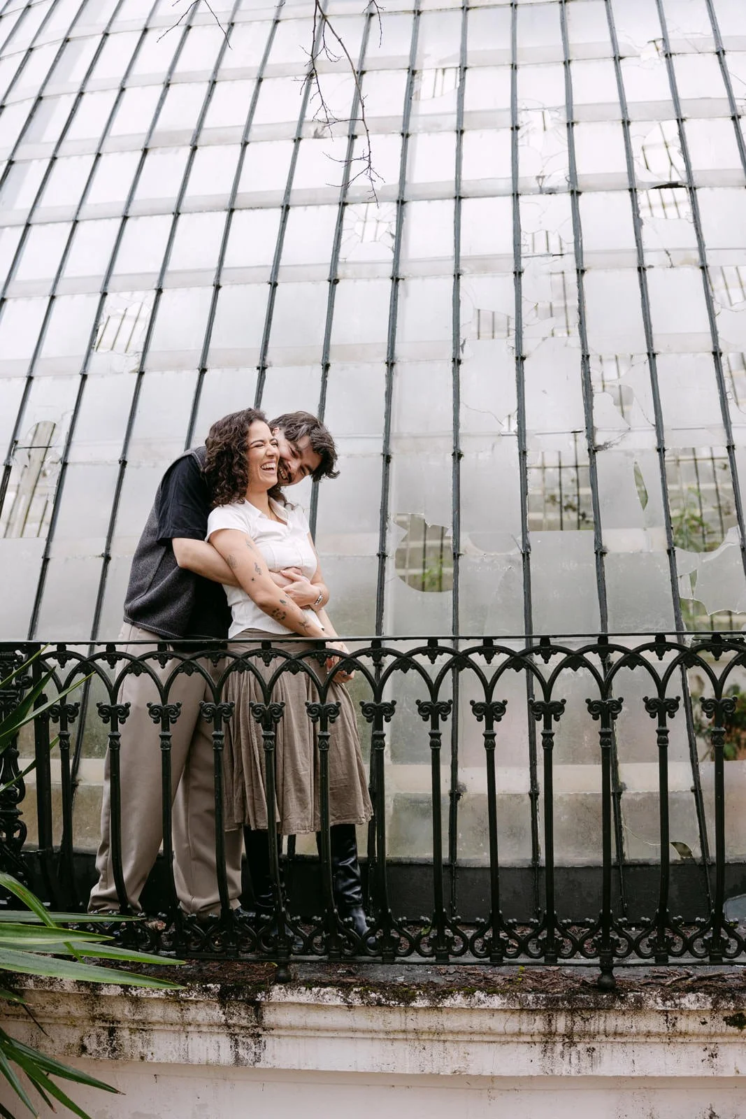 Engaged couple cuddling in front of the Tapada das Necessidades greenhouse in Lisbon