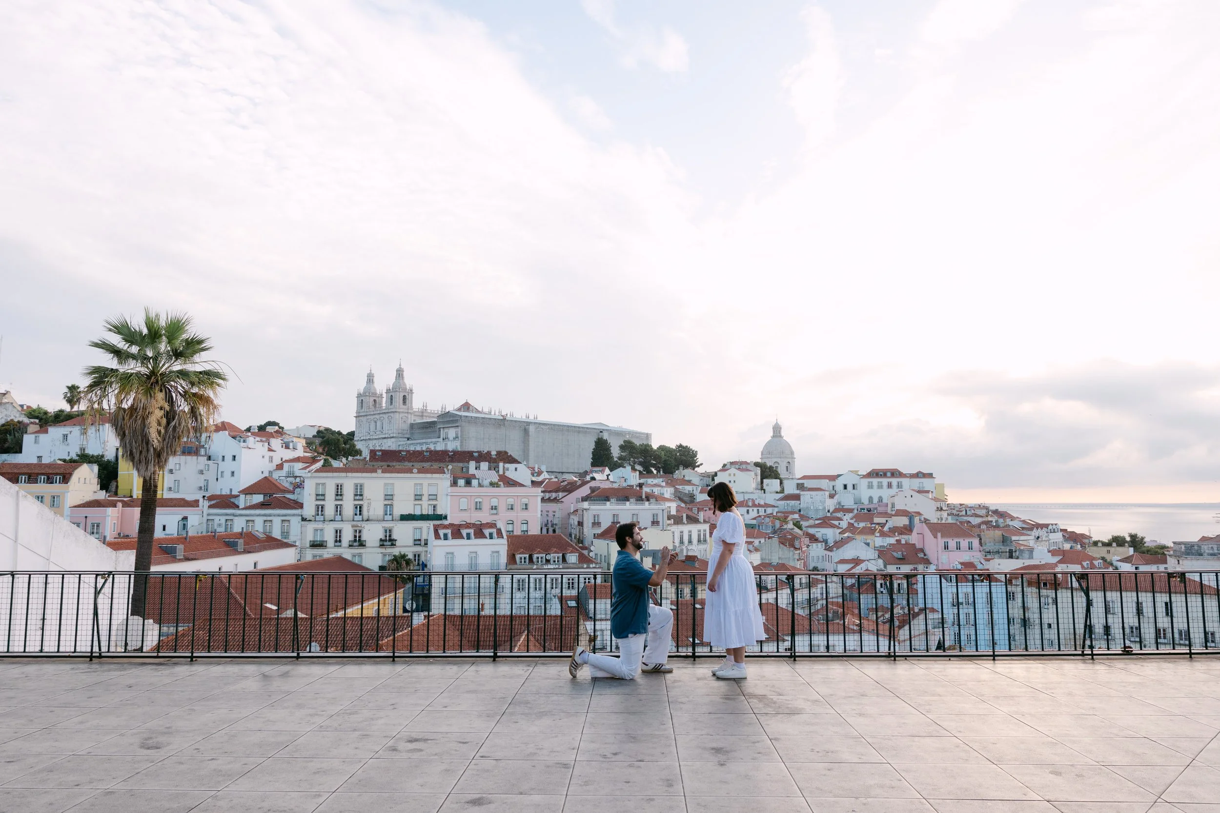 Wide view of a sunrise surprise proposal at Portas do Sol with the rooftops of Alfama in the background.