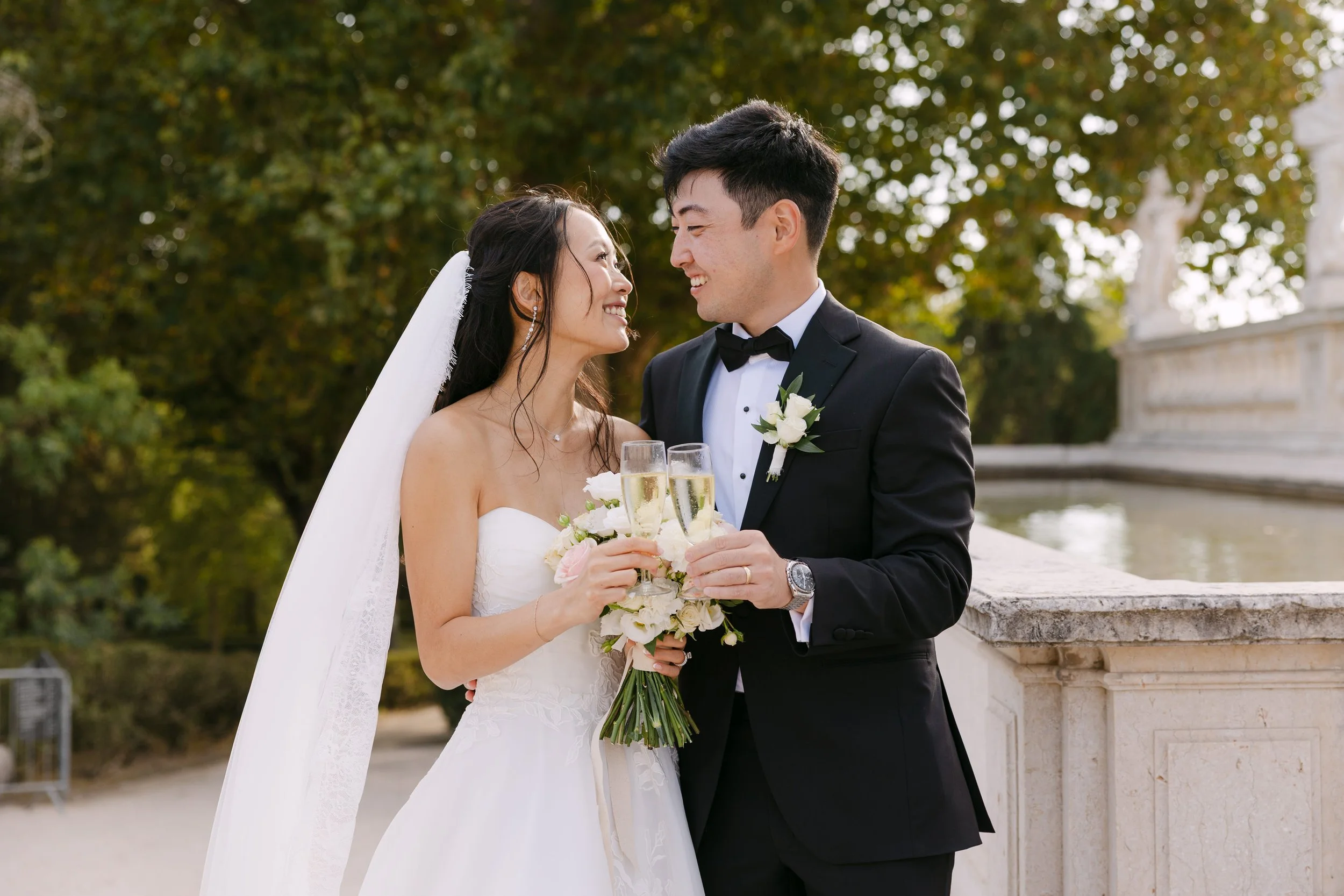 Newlyweds smiling at each other and raising glasses of champagne after their ceremony in the gardens of Palácio Nacional de Queluz.