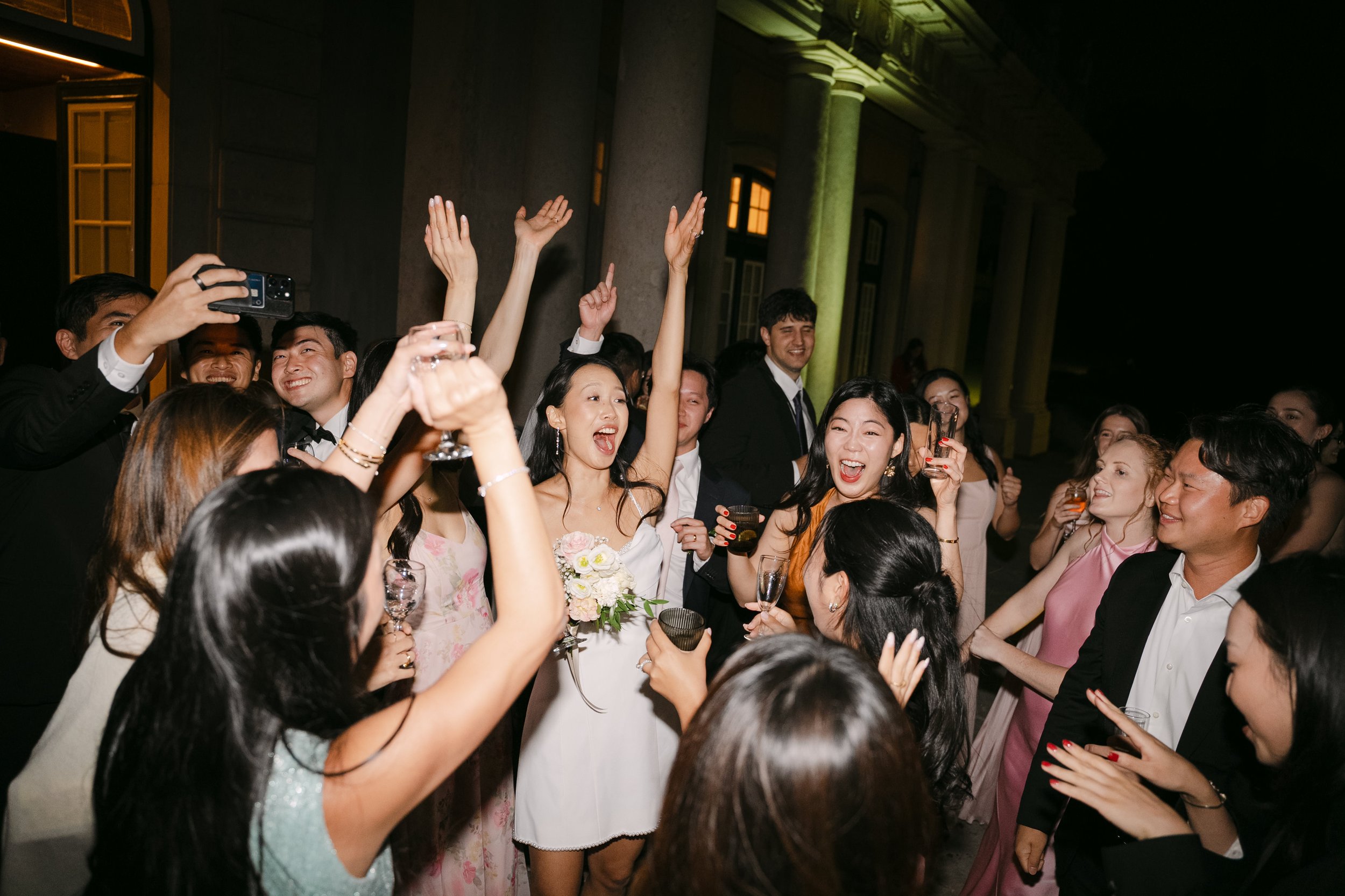 Bride and groom surrounded by cheering friends with hands in the air during a packed wedding dance floor at Palácio Nacional de Queluz.