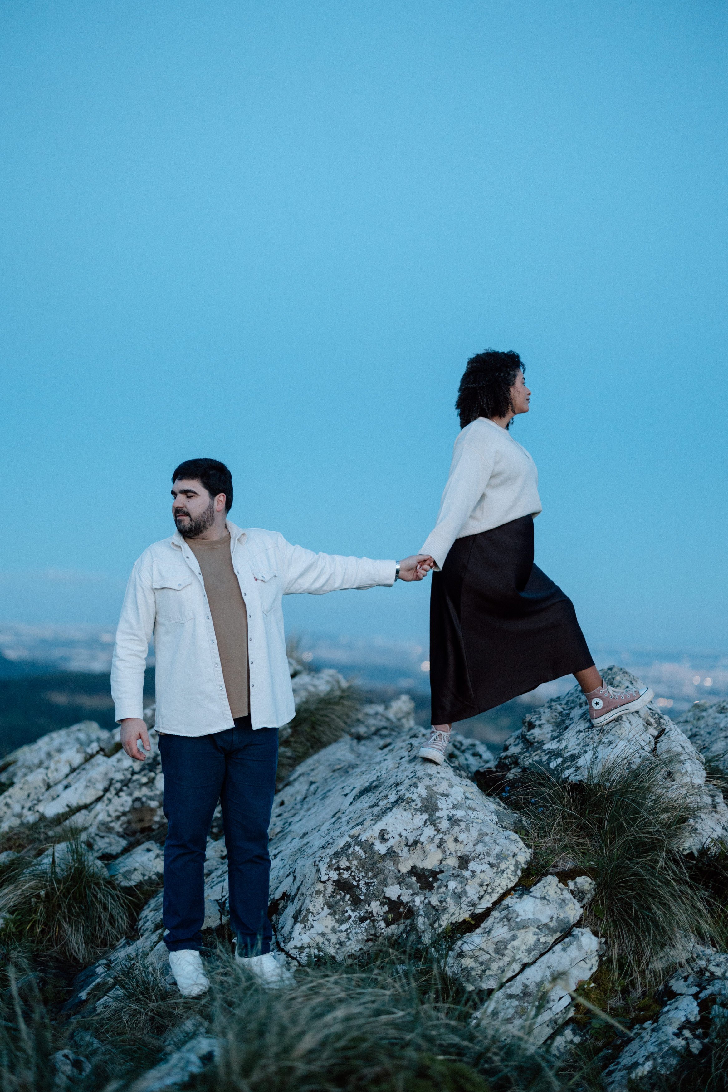 Couple holding hands on rocky cliffs during sunset engagement session in Sintra