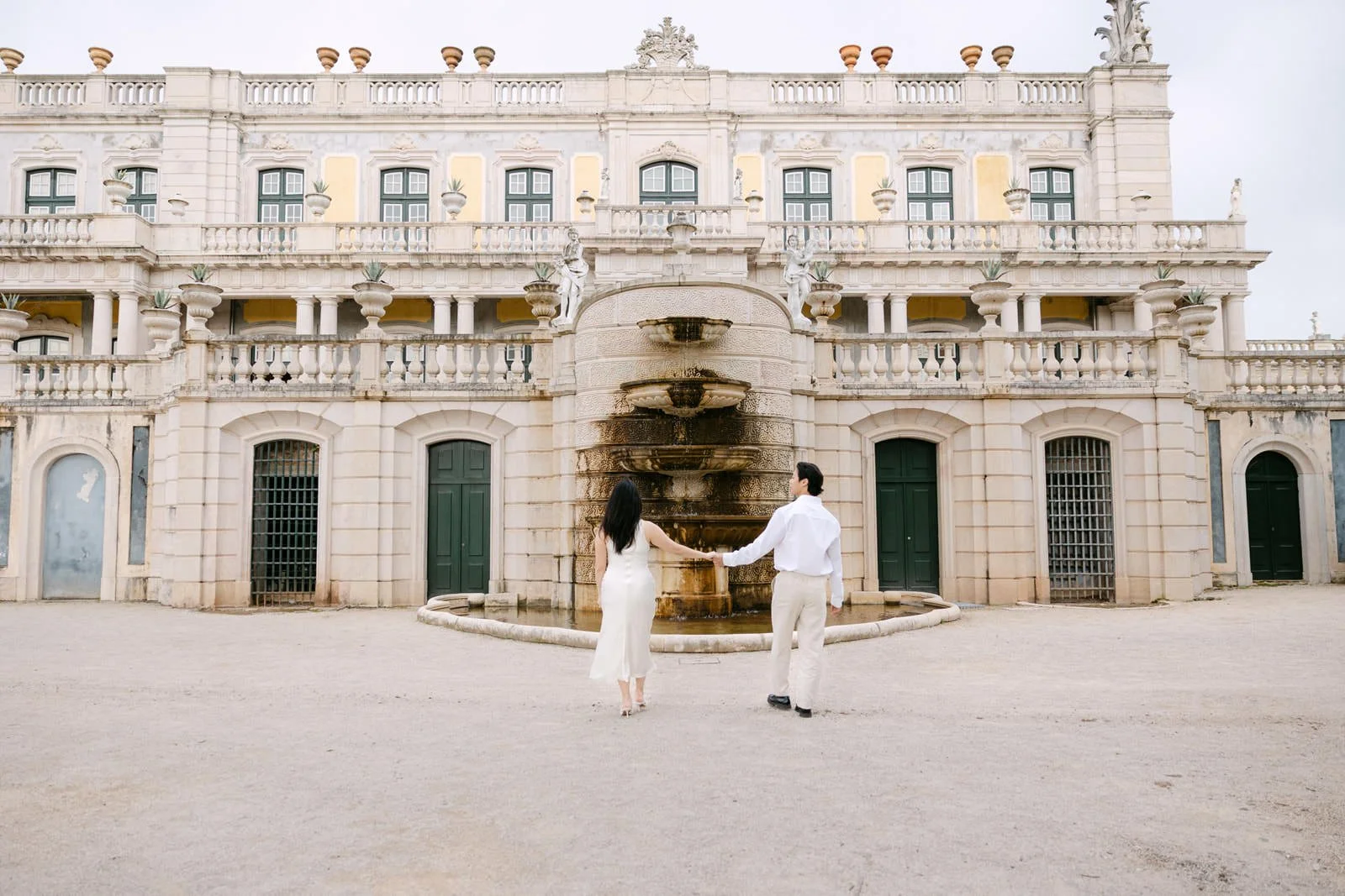 Couple walking through the historic courtyard of Palácio de Queluz during engagement photos.