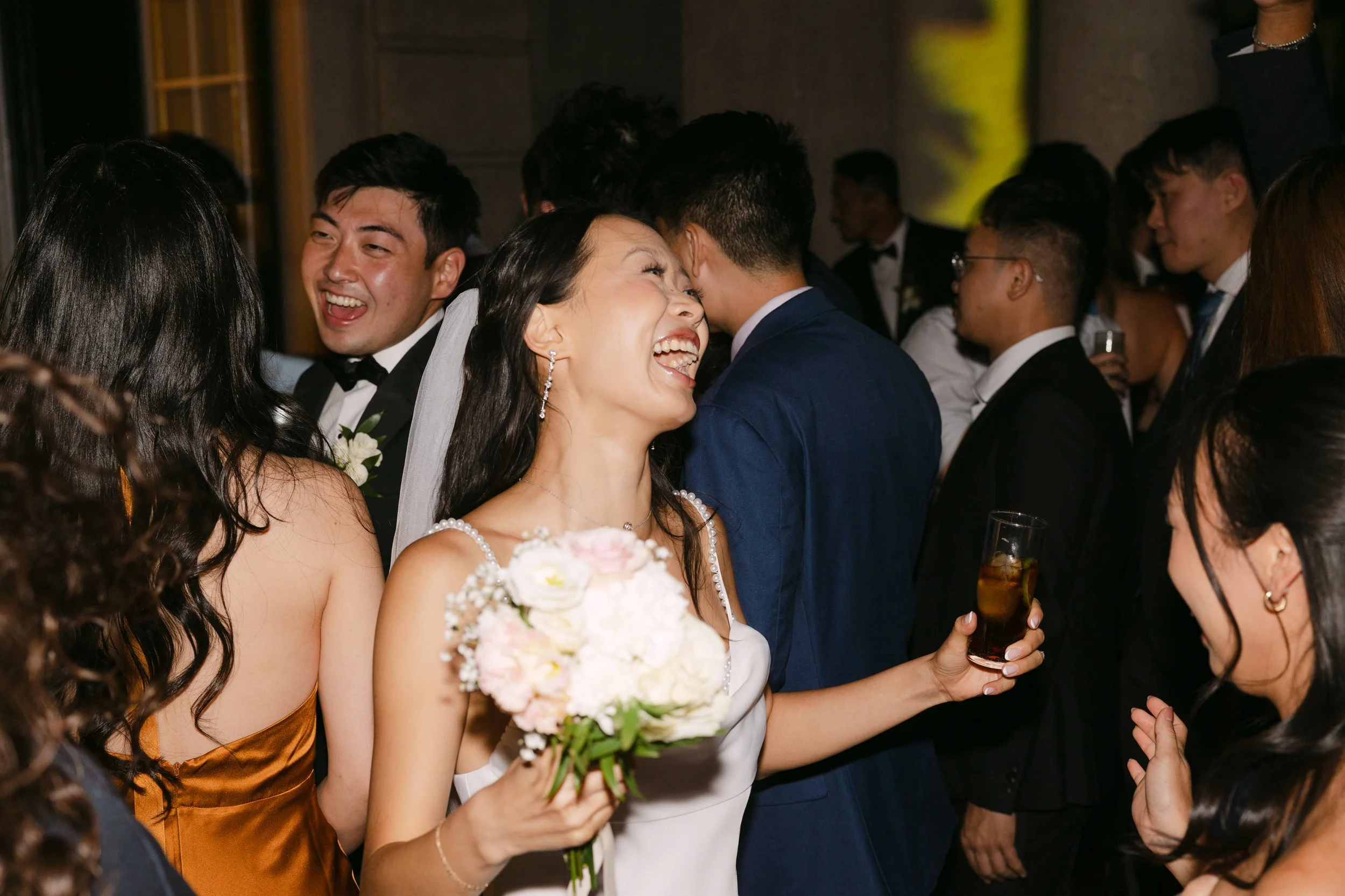 Bride laughing with her bouquet and a drink in hand while celebrating with friends on the dance floor at Palácio Nacional de Queluz.