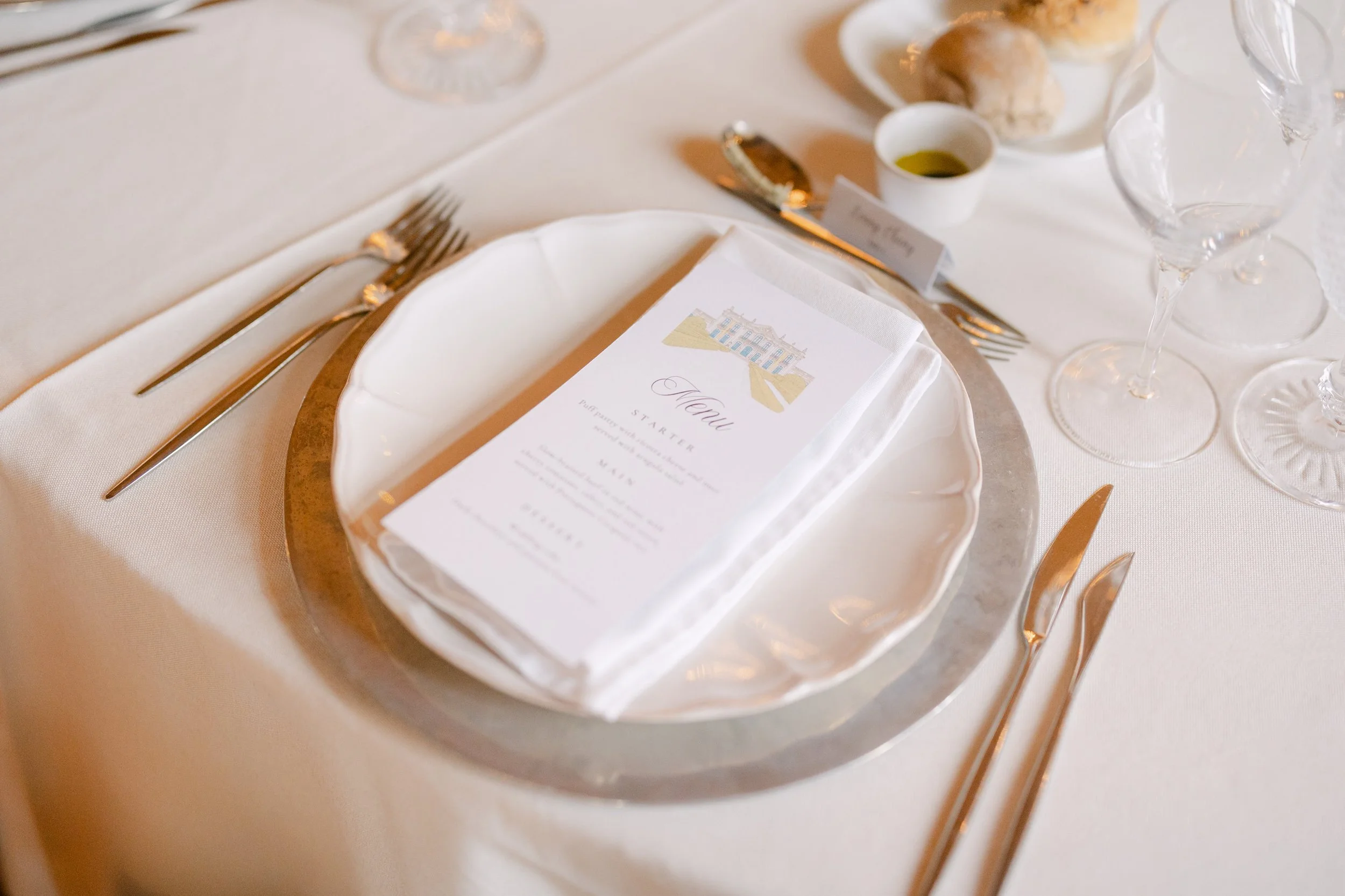 Elegant wedding place setting with a printed menu, white linens, glassware and gold-toned cutlery at the reception inside Palácio Nacional de Queluz.