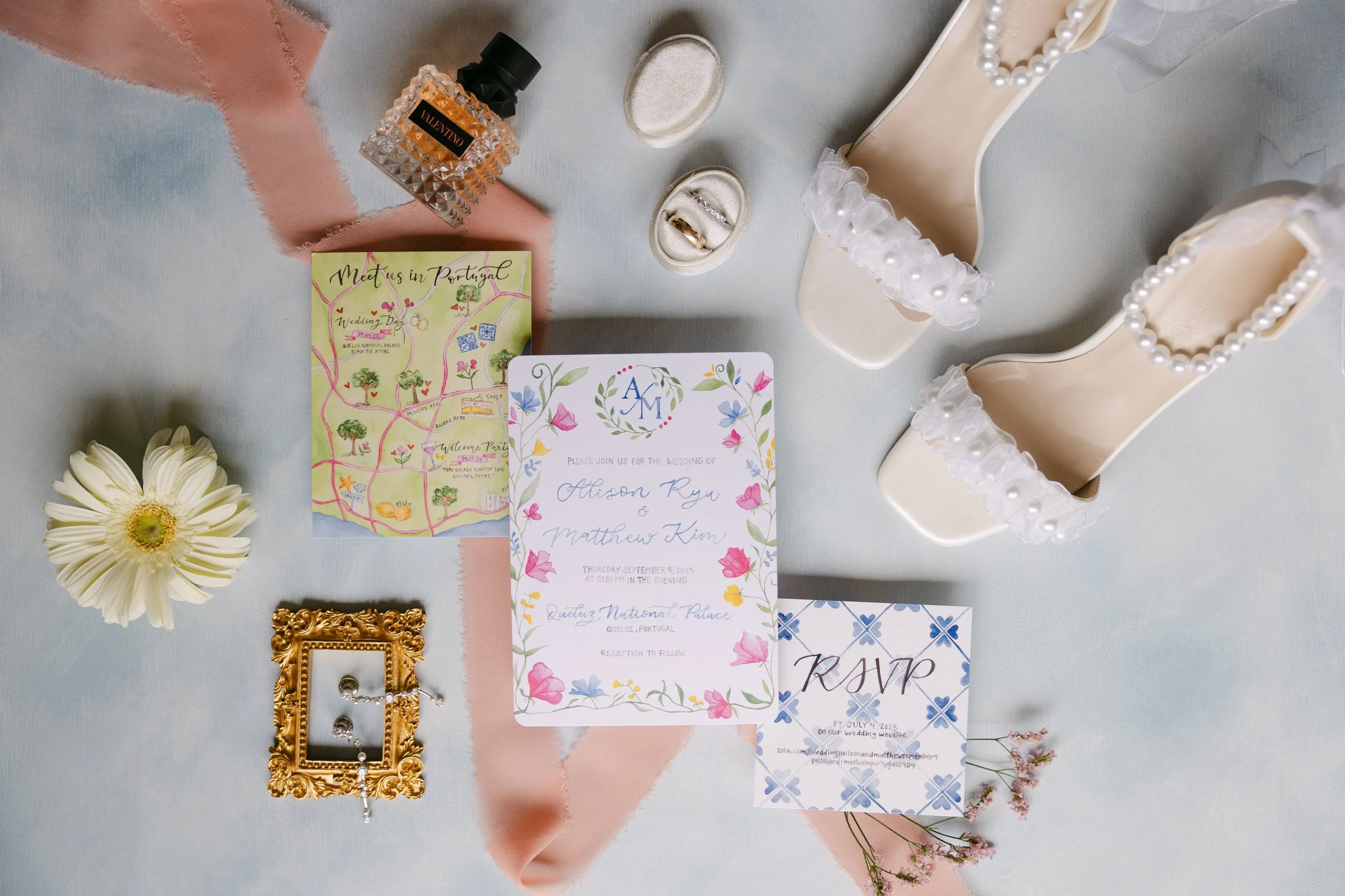 Colourful wedding details arranged in a playful editorial flat lay with pearl bridal shoes, wedding rings, perfume, stationery, flowers and a small framed photograph for a wedding at Palácio Nacional de Queluz.