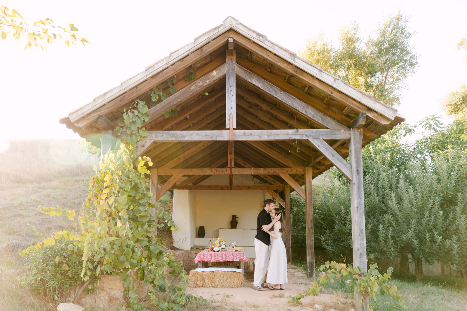 Newly engaged couple kissing beneath a rustic wooden shelter after their surprise proposal at Quinta de Sant’Ana in the Portuguese countryside.
