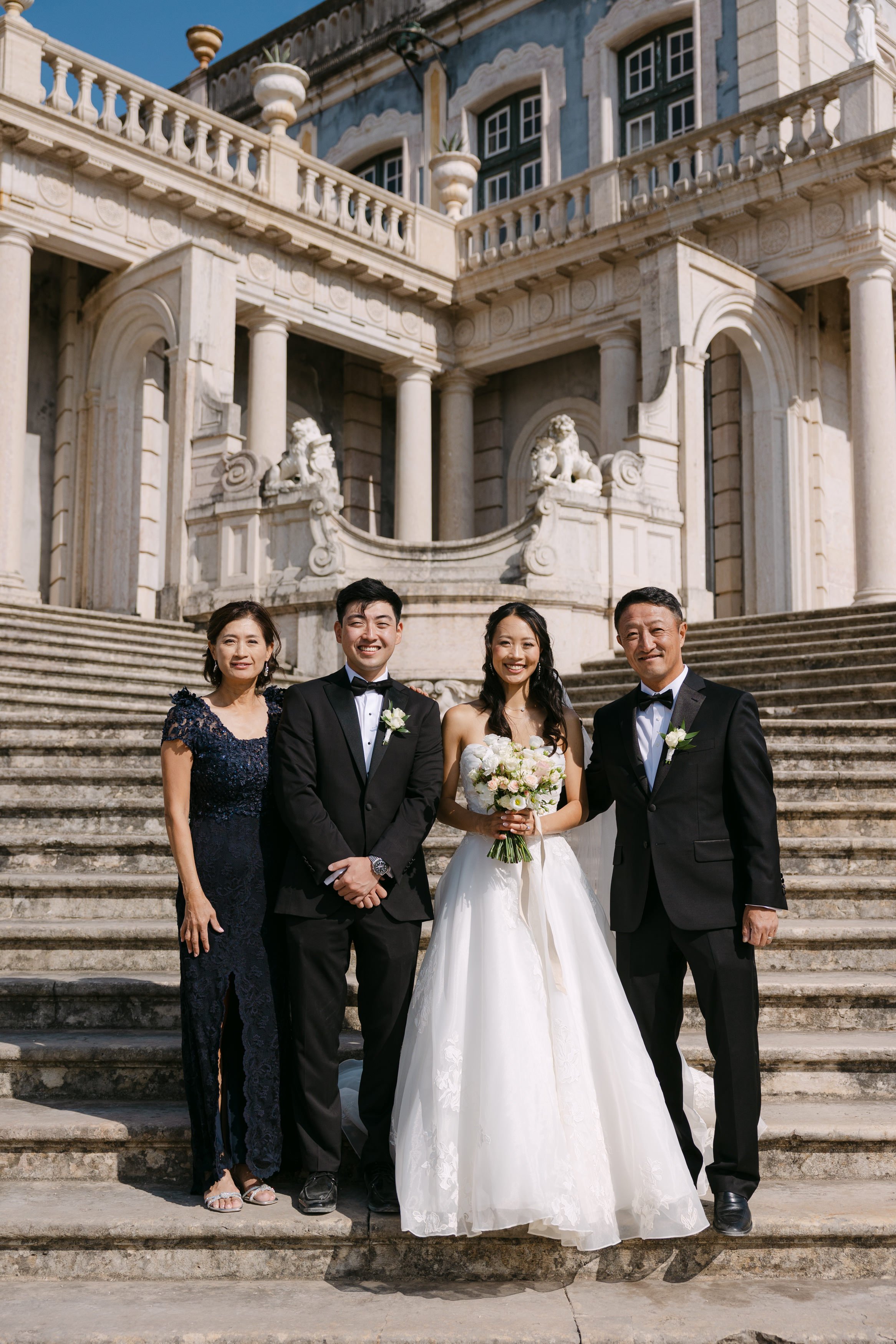Bride and groom posing with the groom’s family on the grand staircase at Palácio Nacional de Queluz before the wedding ceremony.