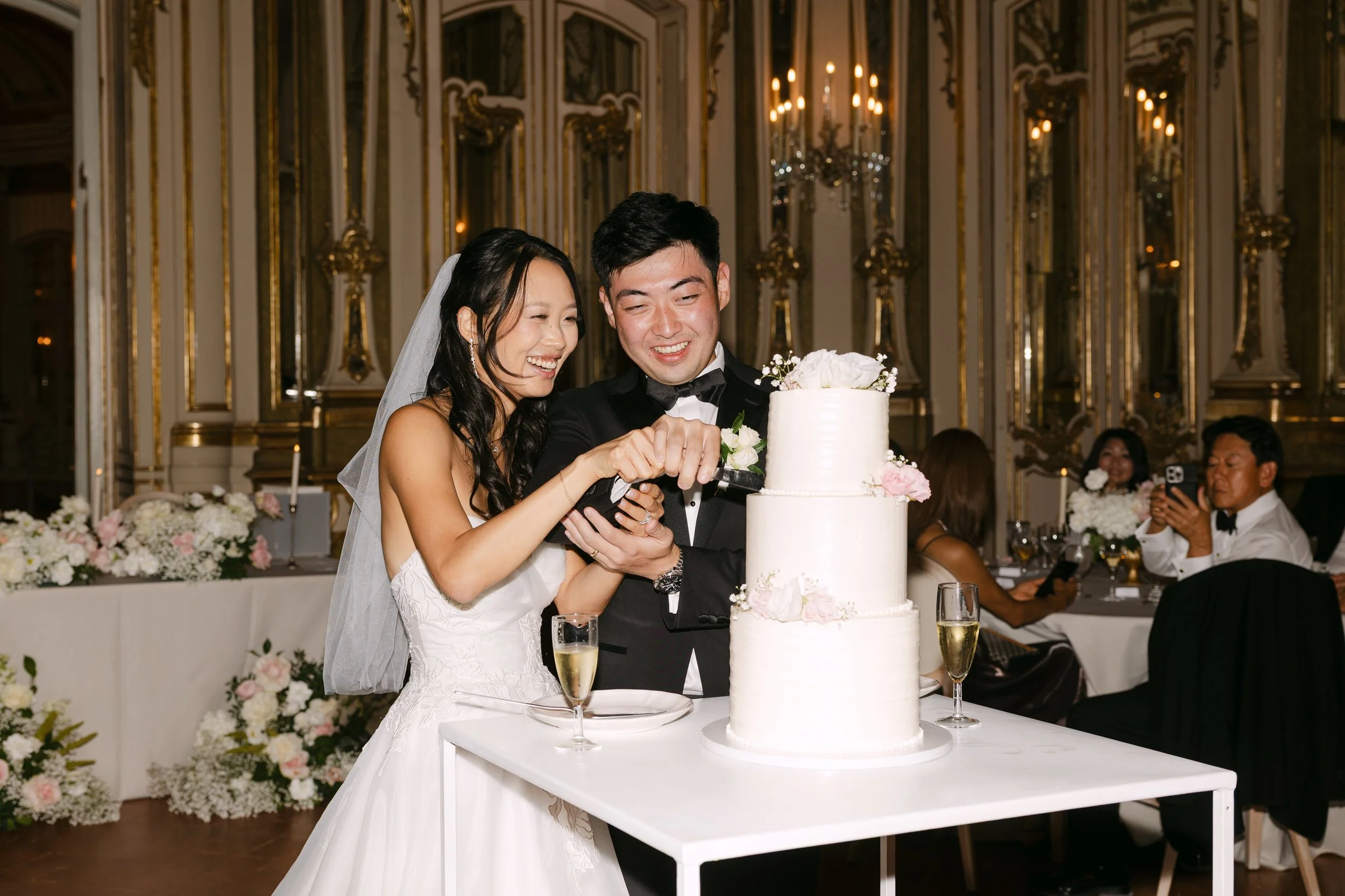 Bride and groom laughing together as they cut their three-tier wedding cake during their reception inside Palácio Nacional de Queluz.