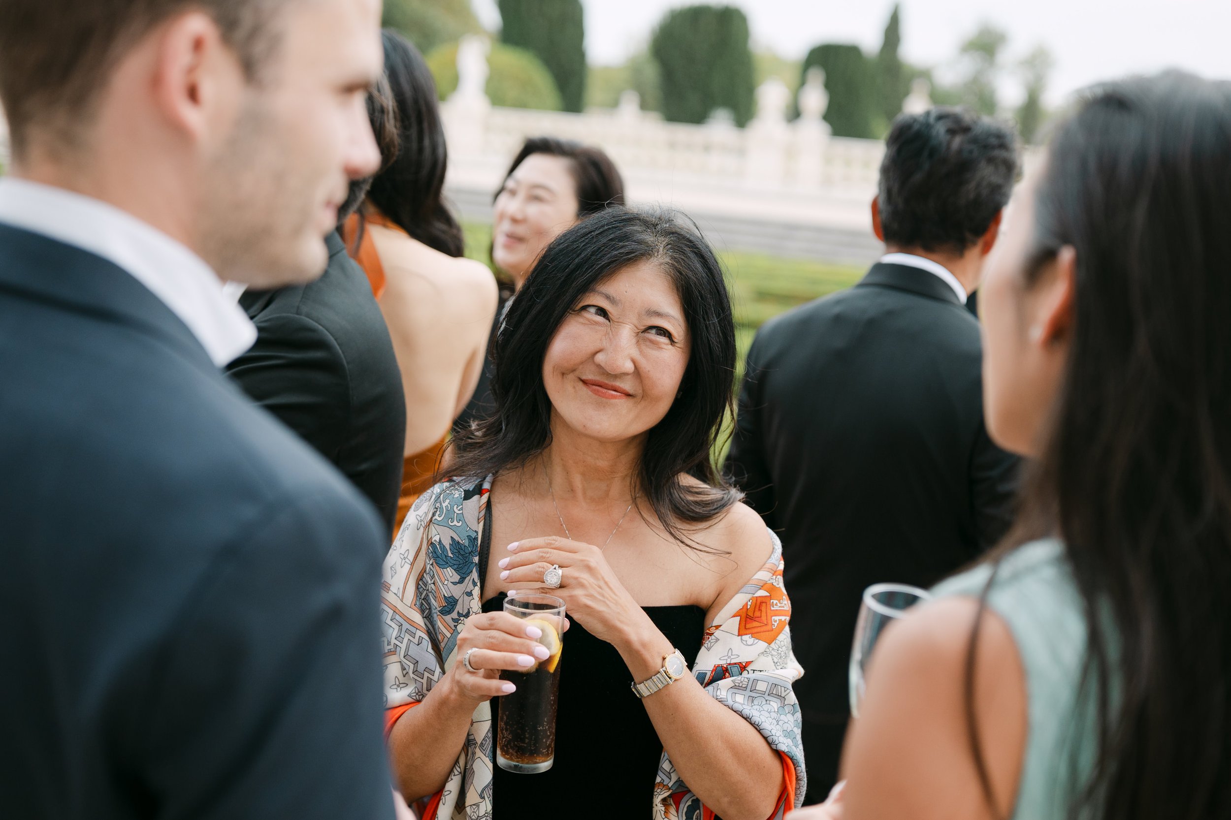 Wedding guest smiling during a candid conversation at the outdoor cocktail hour following the ceremony at Palácio Nacional de Queluz.