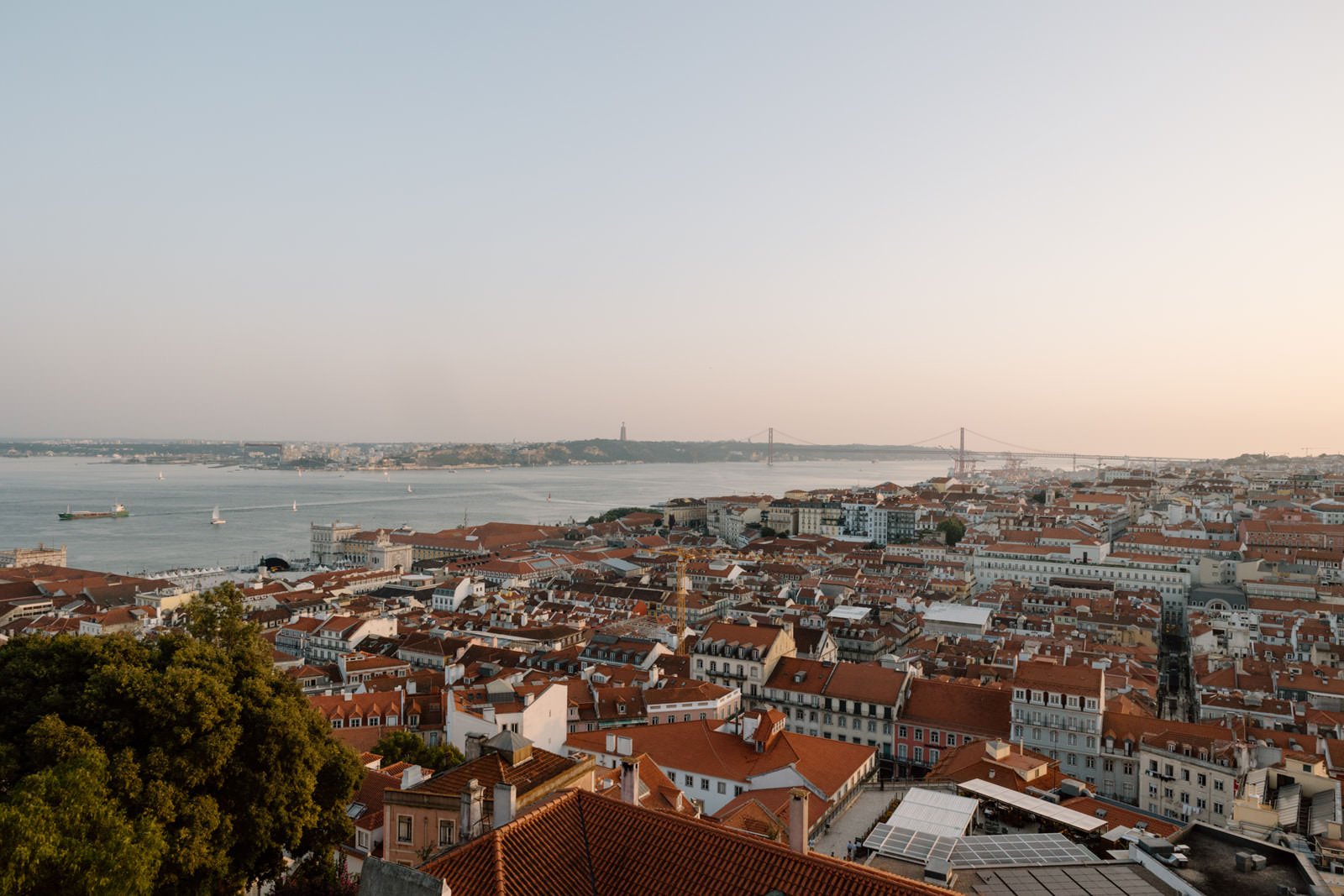 Happy couple embracing during a sunset engagement session at Castelo de São Jorge with Lisbon in the background.