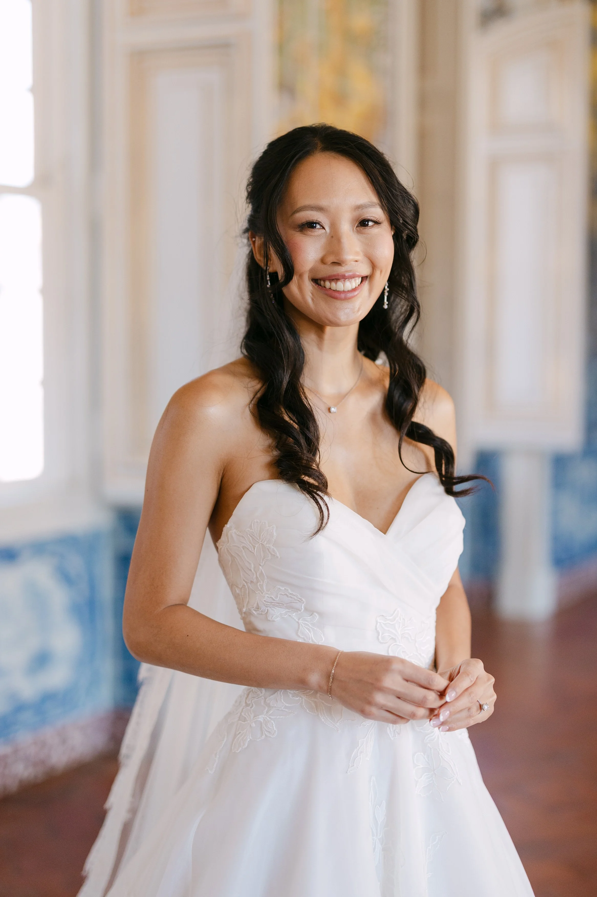 Bride smiling in her white wedding gown during a softly lit portrait inside Palácio Nacional de Queluz before the ceremony.