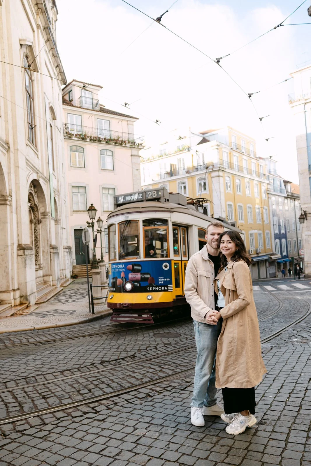 Couple photographed beside a passing yellow tram in Lisbon Portugal