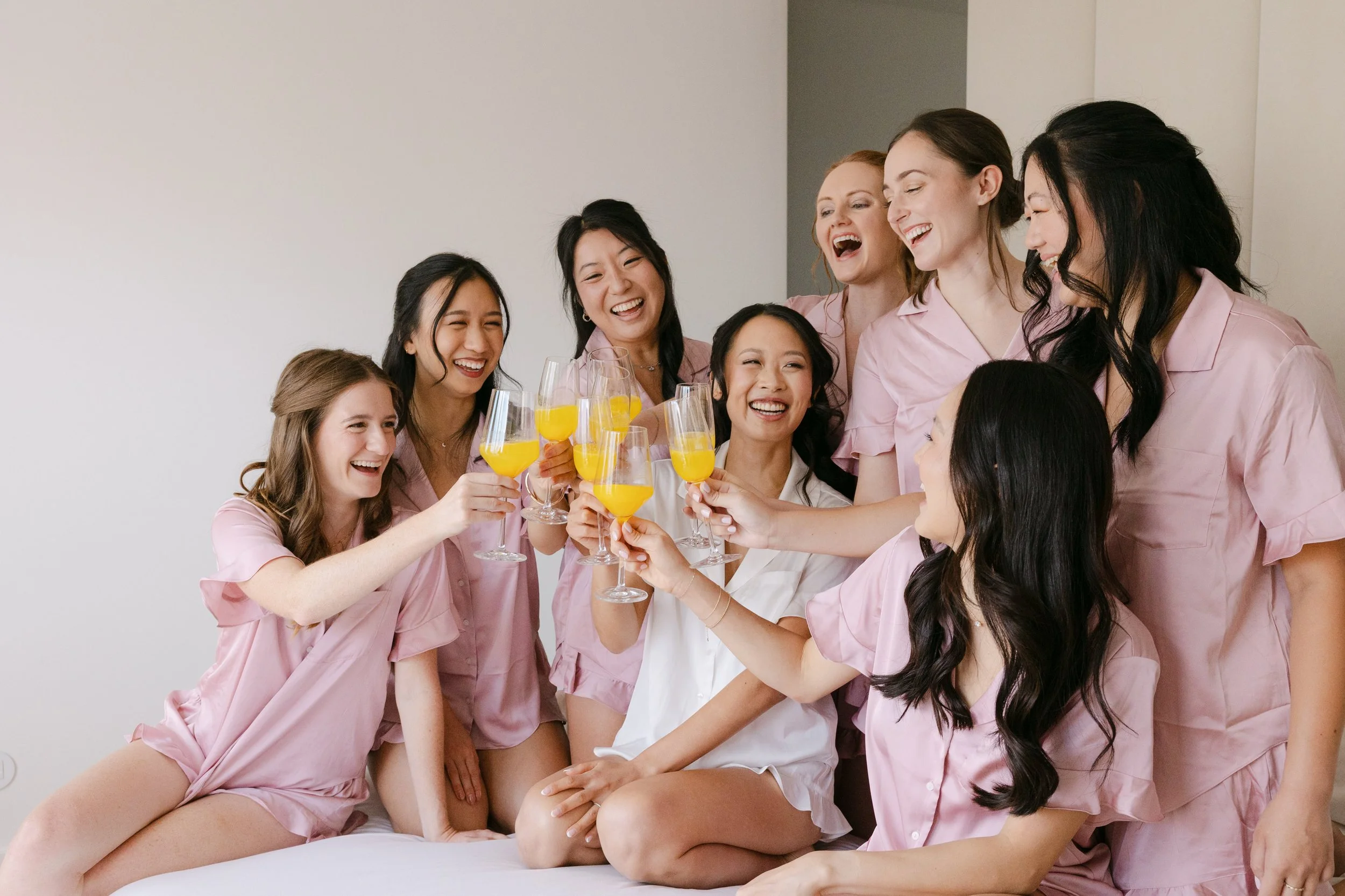 Bride and bridesmaids laughing and raising their glasses together during a joyful wedding morning toast in Lisbon, Portugal.