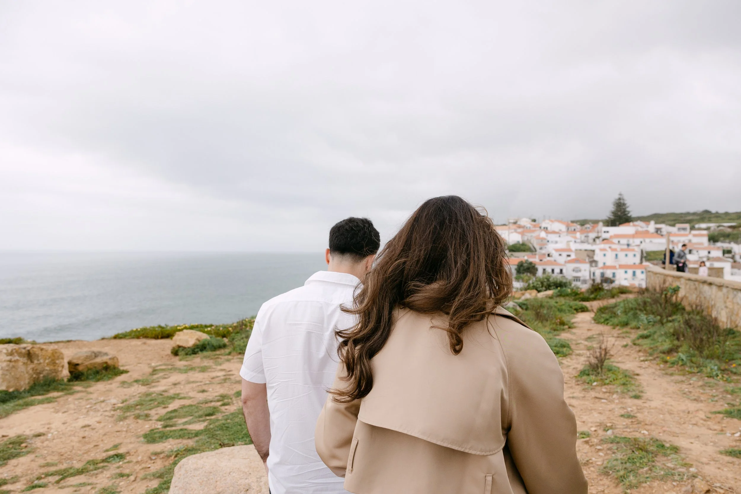 Couple walking towards the cliffs of Azenhas do Mar during romantic engagement session in Portugal.