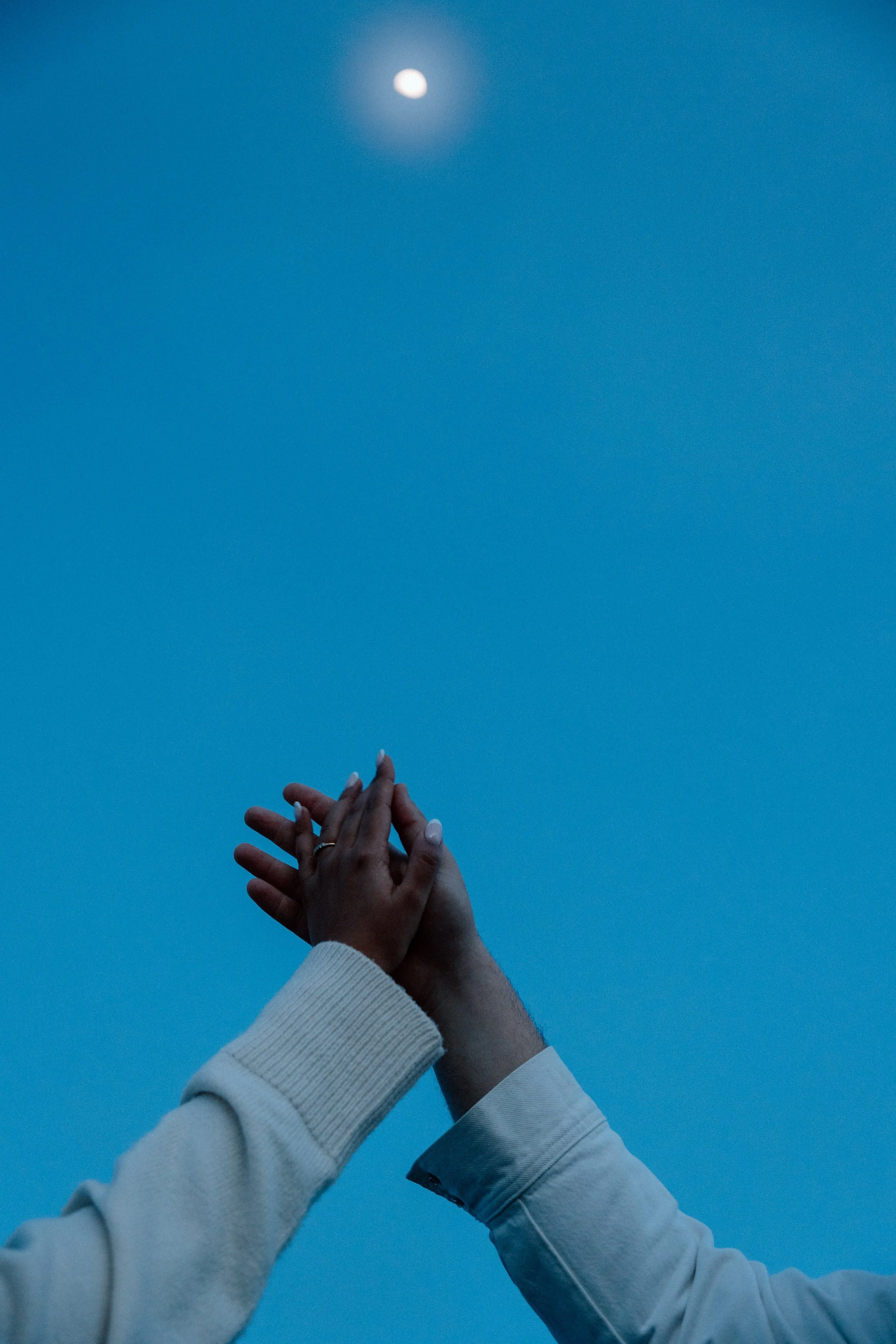 Close-up detail photo of couple holding hands under blue evening sky during engagement session