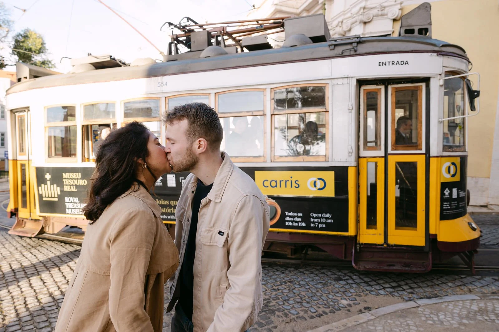 Couple kissing in front of a traditional yellow Lisbon tram after their proposal