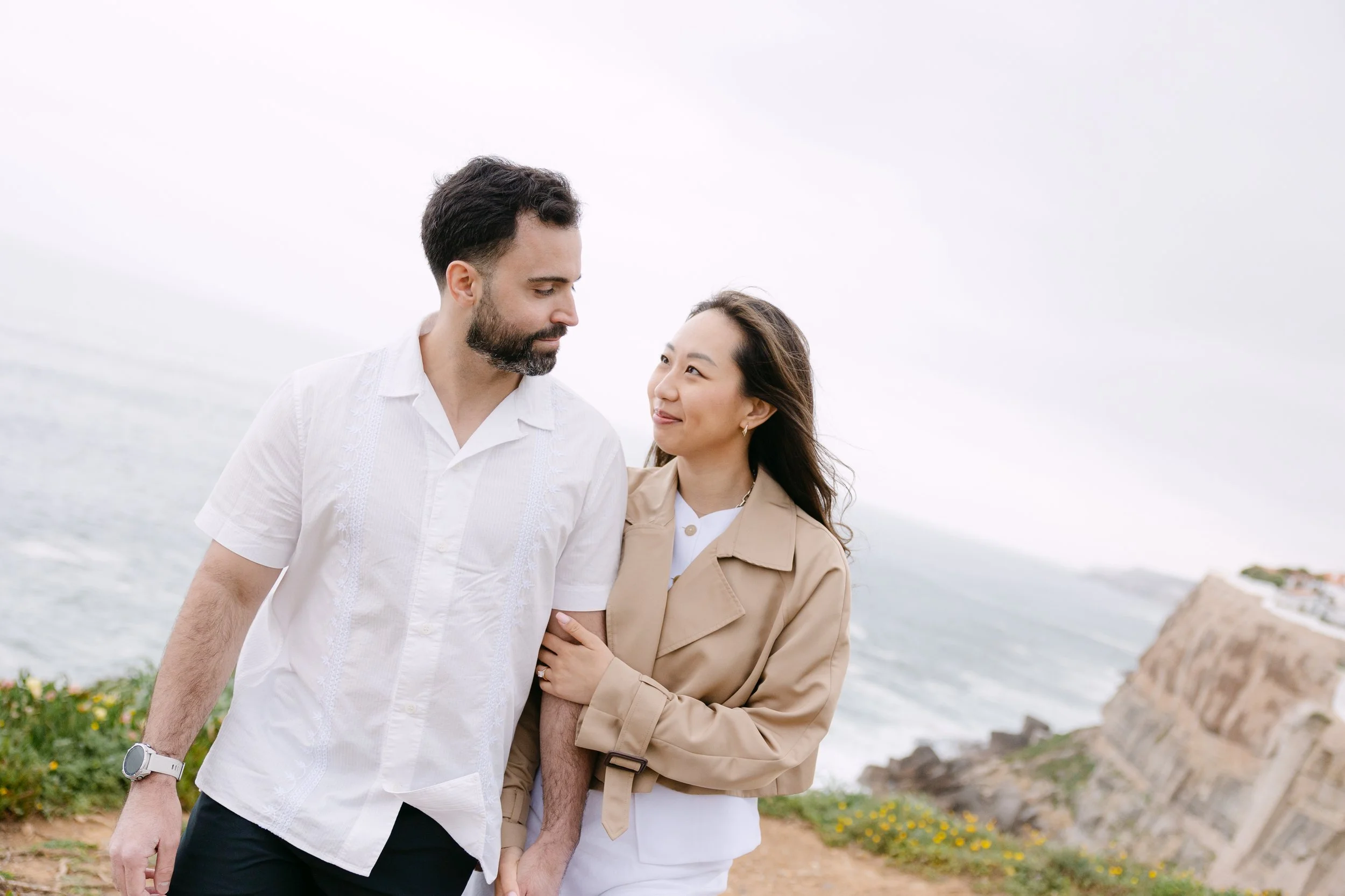 Engaged couple walking together along the cliffs of Azenhas do Mar with Atlantic Ocean views.