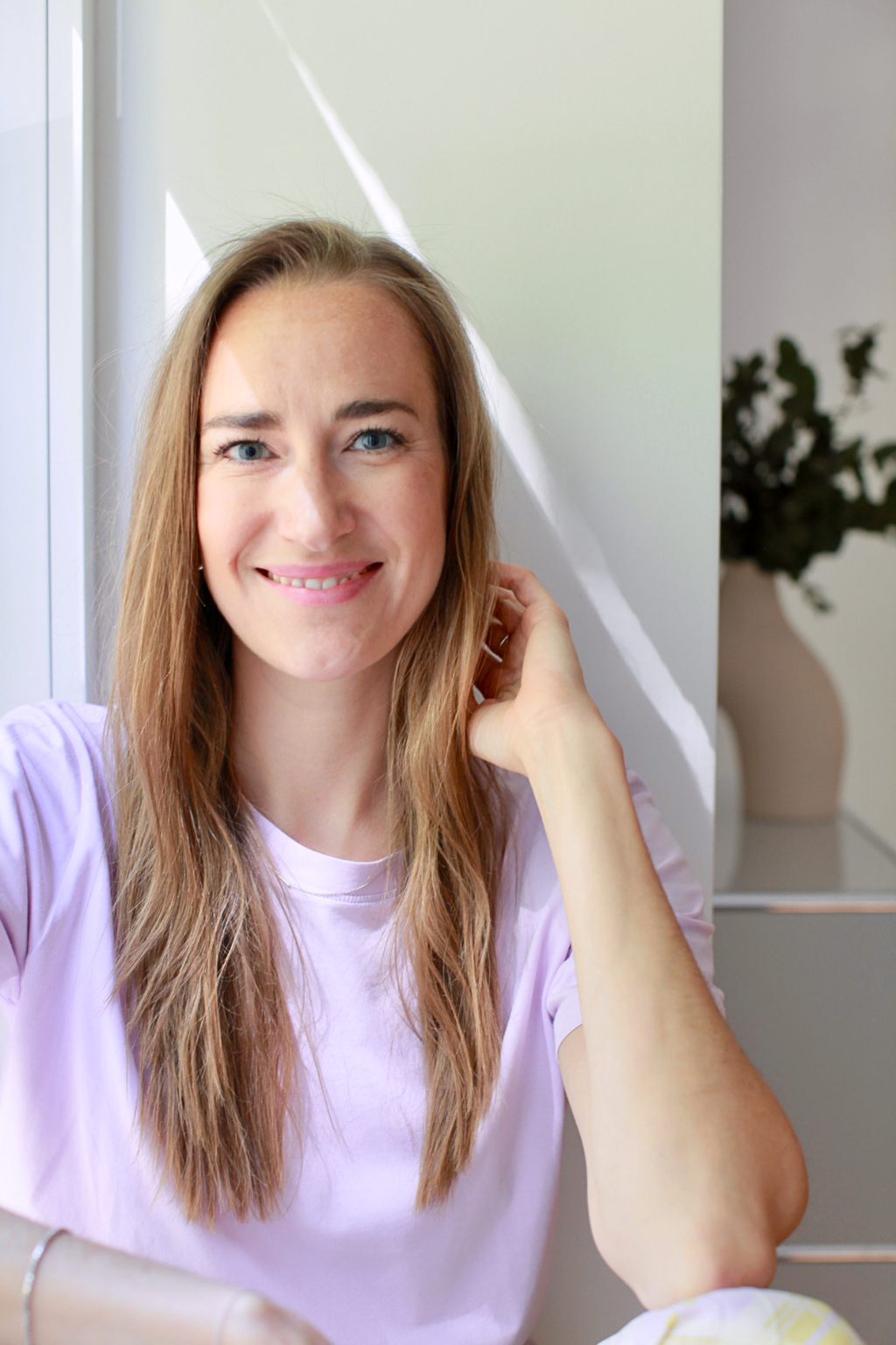 Eine Frau mit langem, dunkelblonden Haar lächelt freundlich, ihr e linke Hand greift locker in die Haare