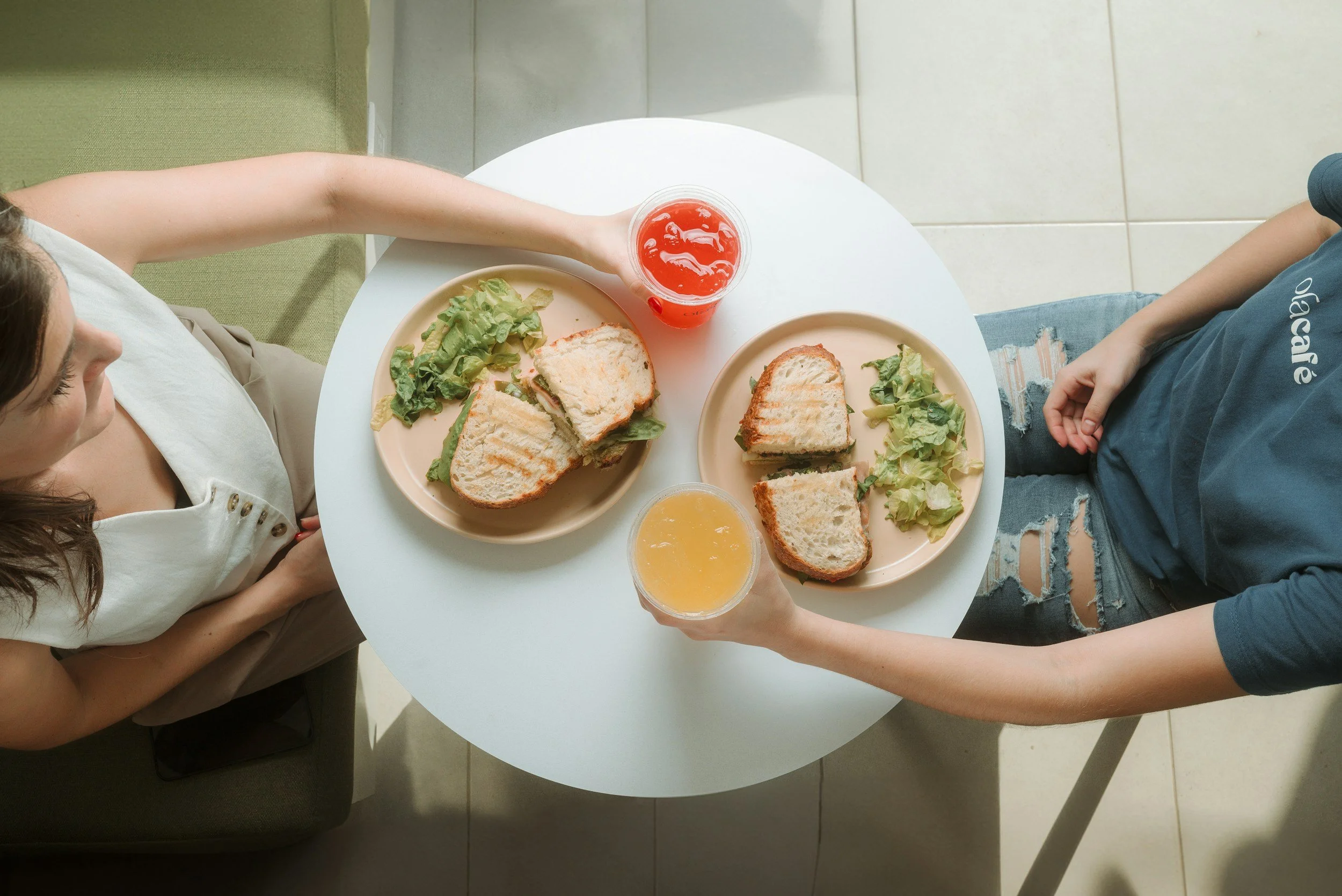 two people eating a meal at a small table in a home kitchen of toasted chicken and veggie sandwiches with a side salad.