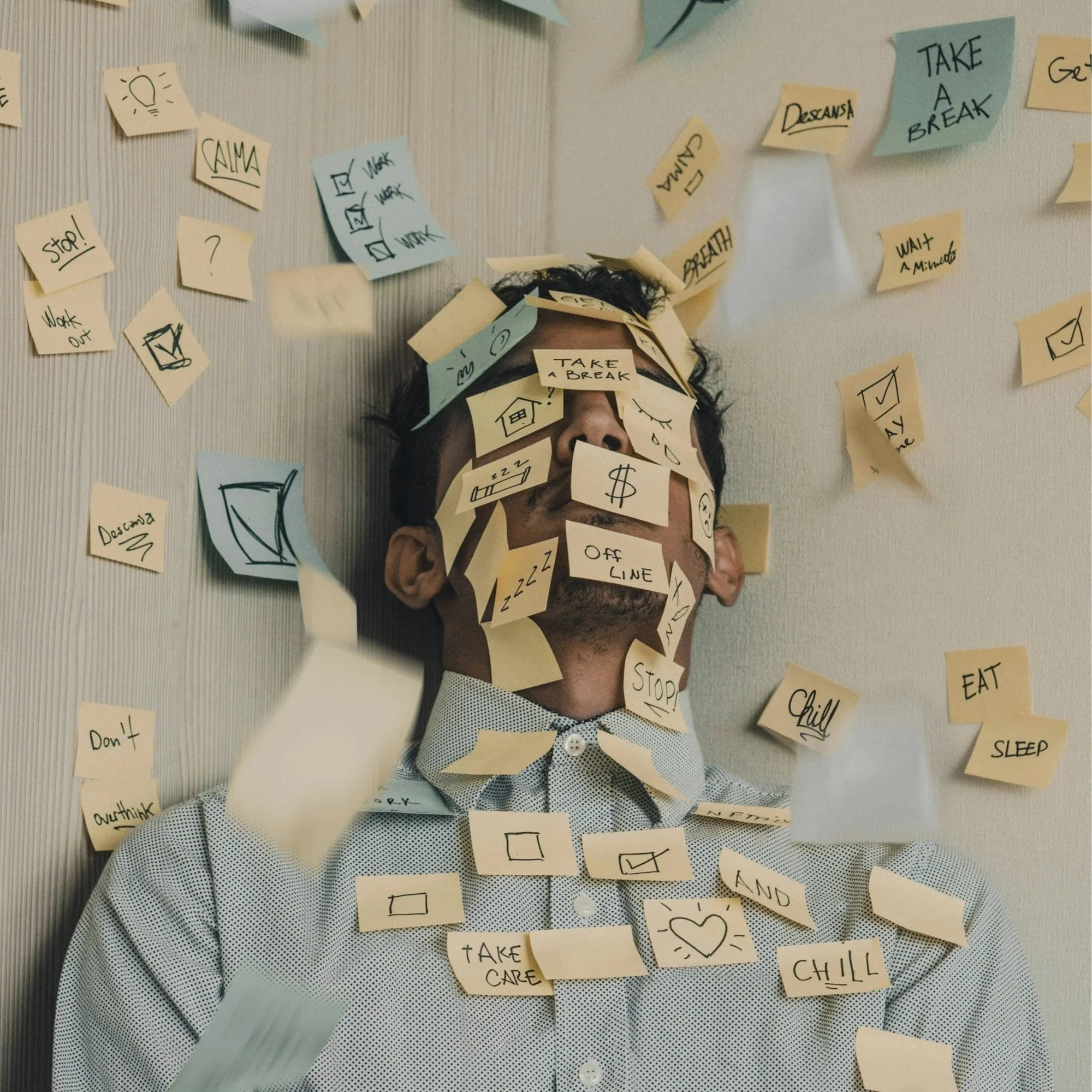 Image of a person with sticky notes all over their head and on the wall surrounding them. Each sticky note has a message such as "work out", "rest", "eat", "breathe", "make money"-signifying the stress and overwhelm of everyday life.