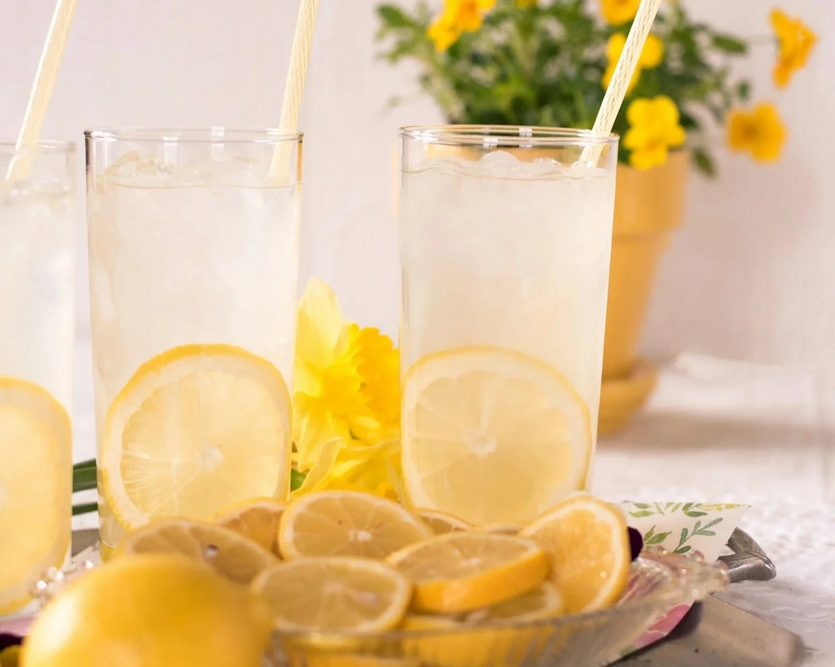 glasses of lemon water along with some sliced lemon on a plate next to the glasses