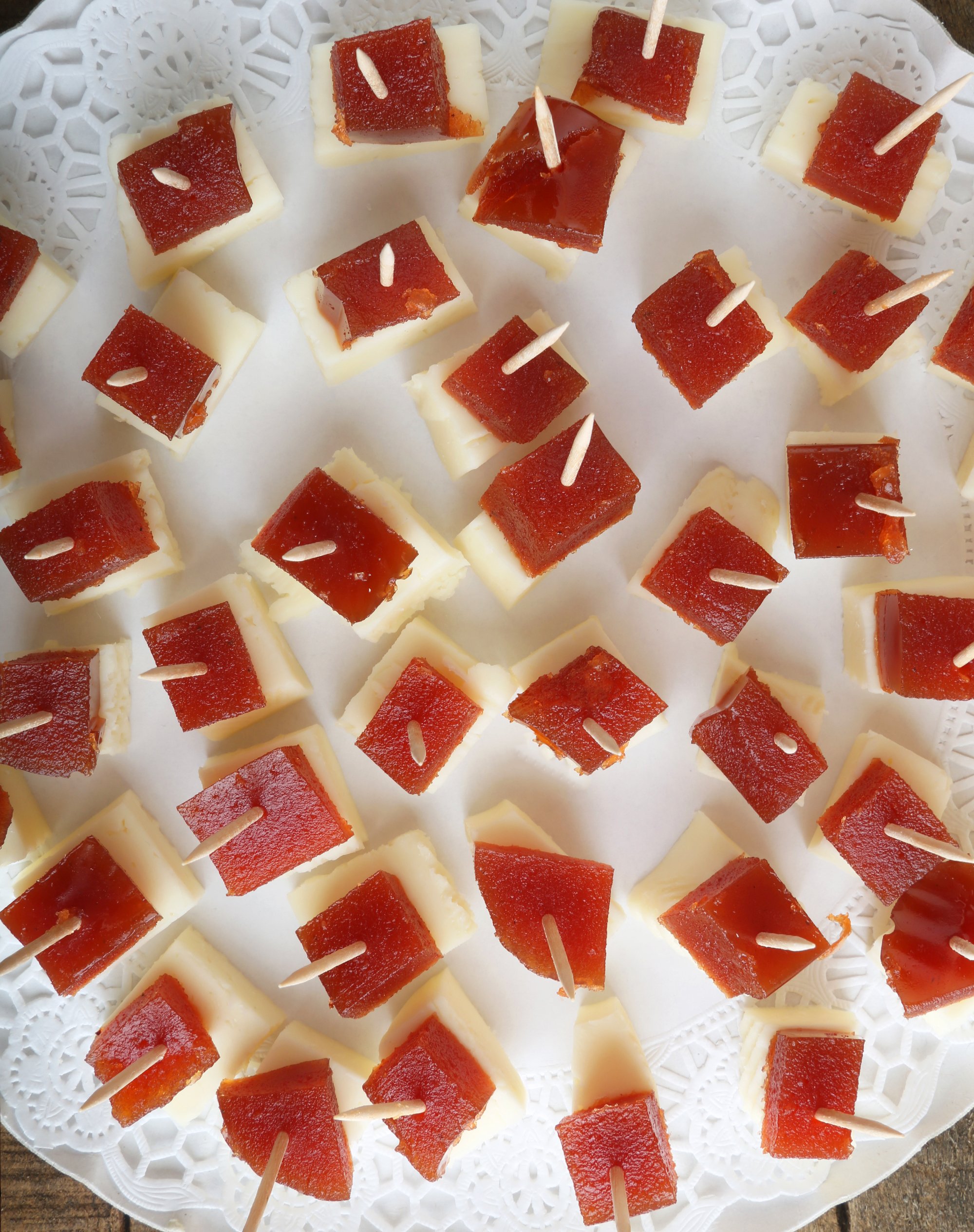 Ponce de Léon Manchego and Membrillo Quince Paste, each secured with a toothpick, arranged on a white doily-lined tray.