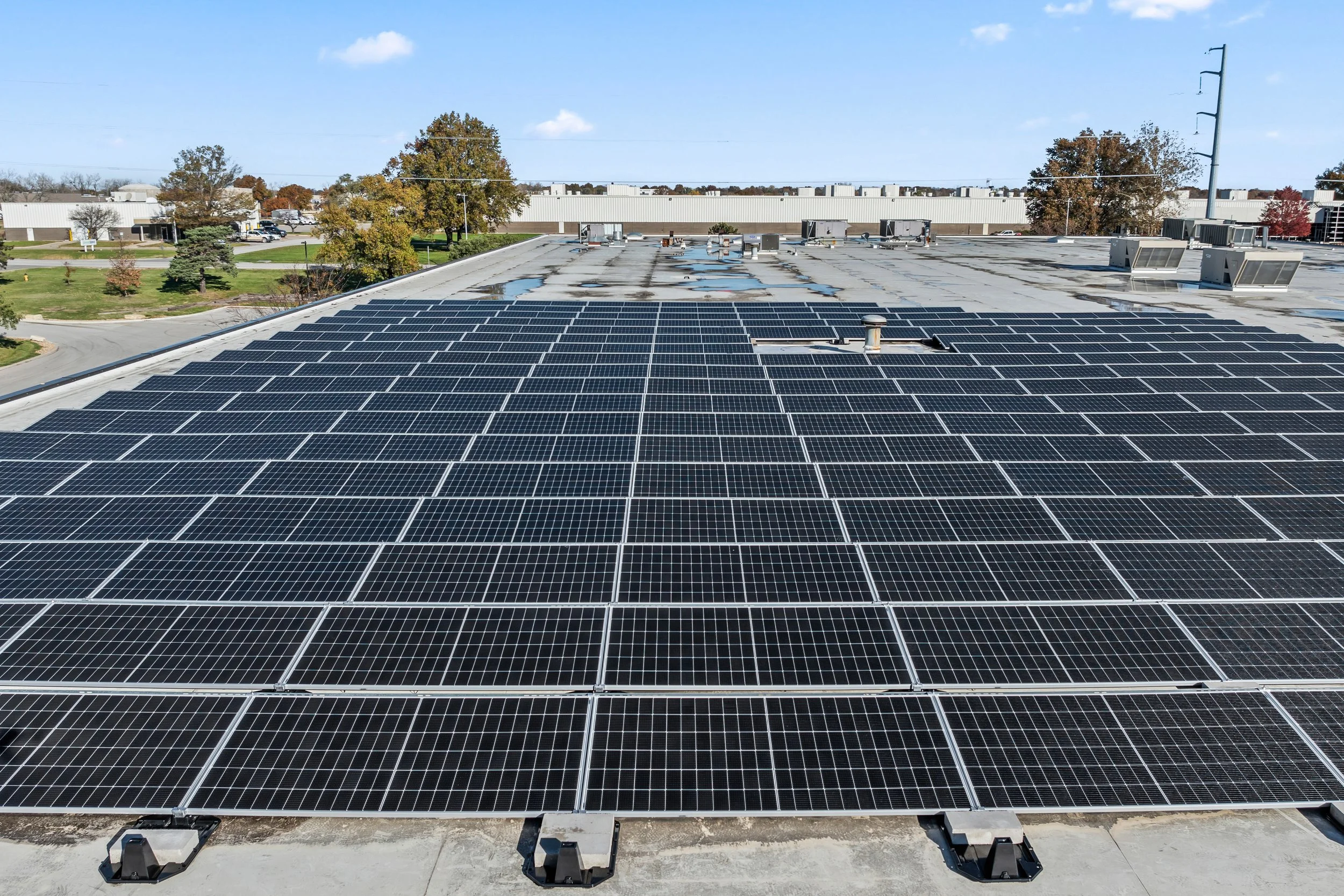 Solar panels installed on a Kansas commercial building roof with a parking lot and trees in the background.
