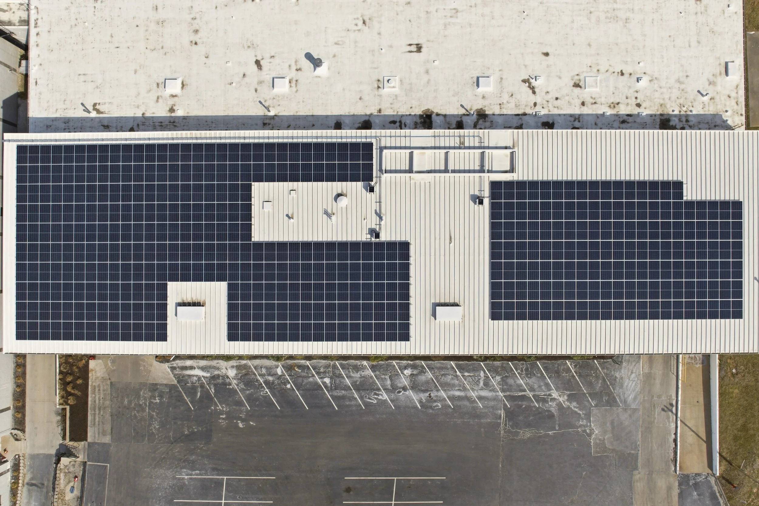 An aerial view of a building in Kansas City, Kansas with 200kW of solar panels on the white roof, and an adjacent empty parking lot.