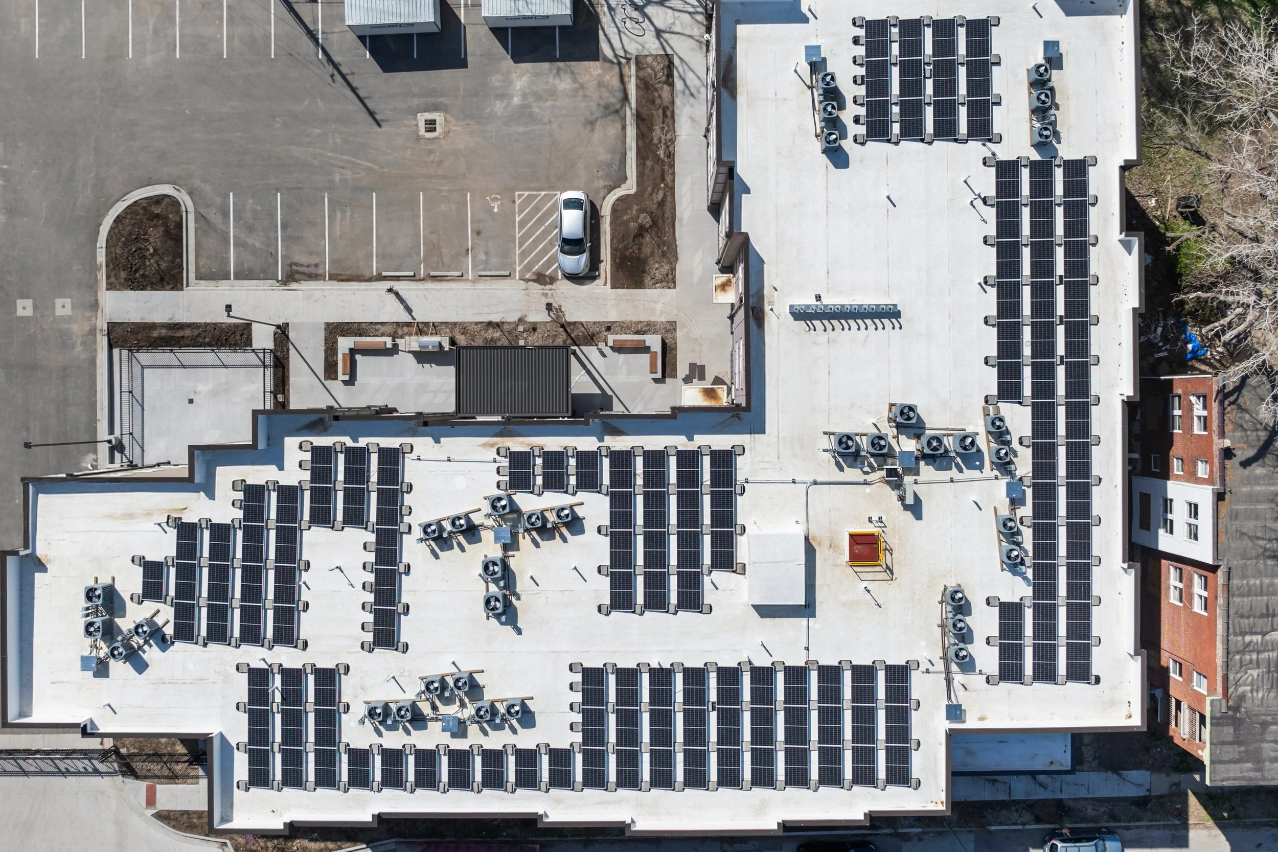 Top-down aerial view of a building rooftop in Kansas City, Missouri featuring multiple solar panel arrays and various HVAC units, with adjacent parking lot and surrounding trees.