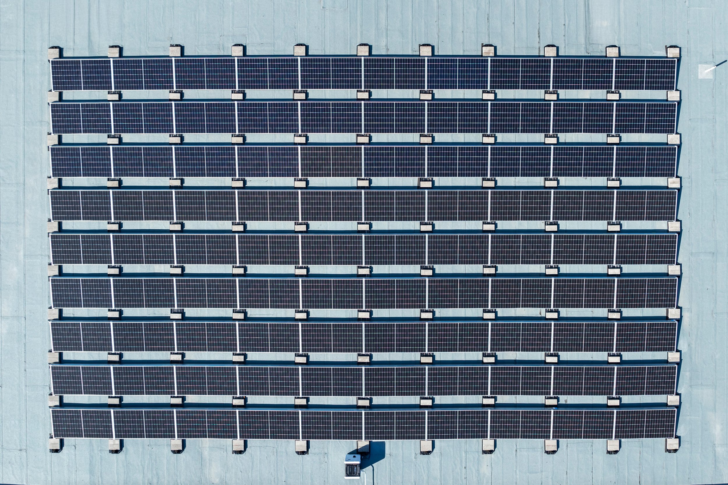 An aerial view of a rooftop with multiple rows of solar panels installed on a flat, light gray surface in Kansas City.