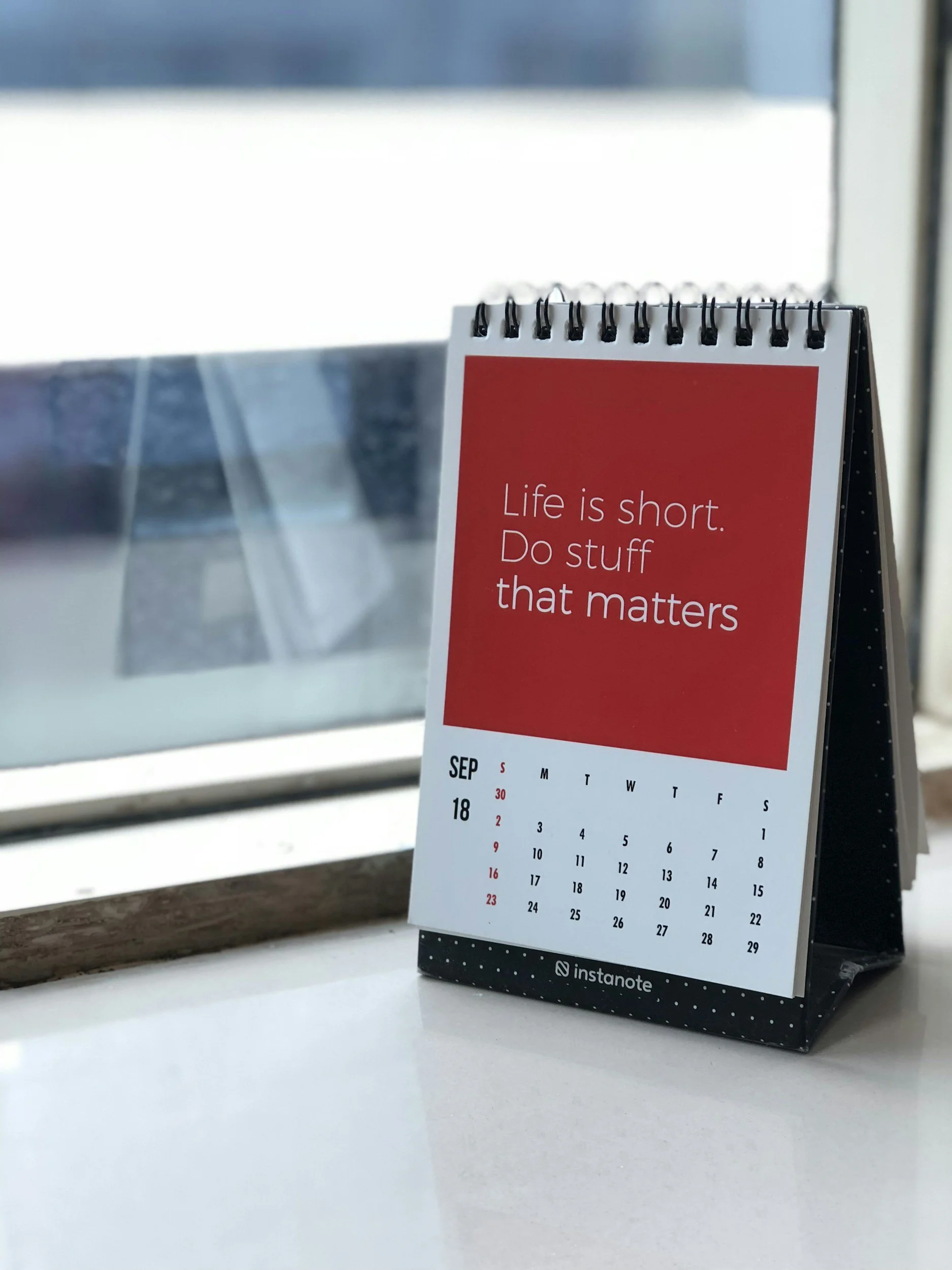 Desk calendar on a table with a motivational quote "Life is short. Do stuff that matters." in a red block above the calendar grid.