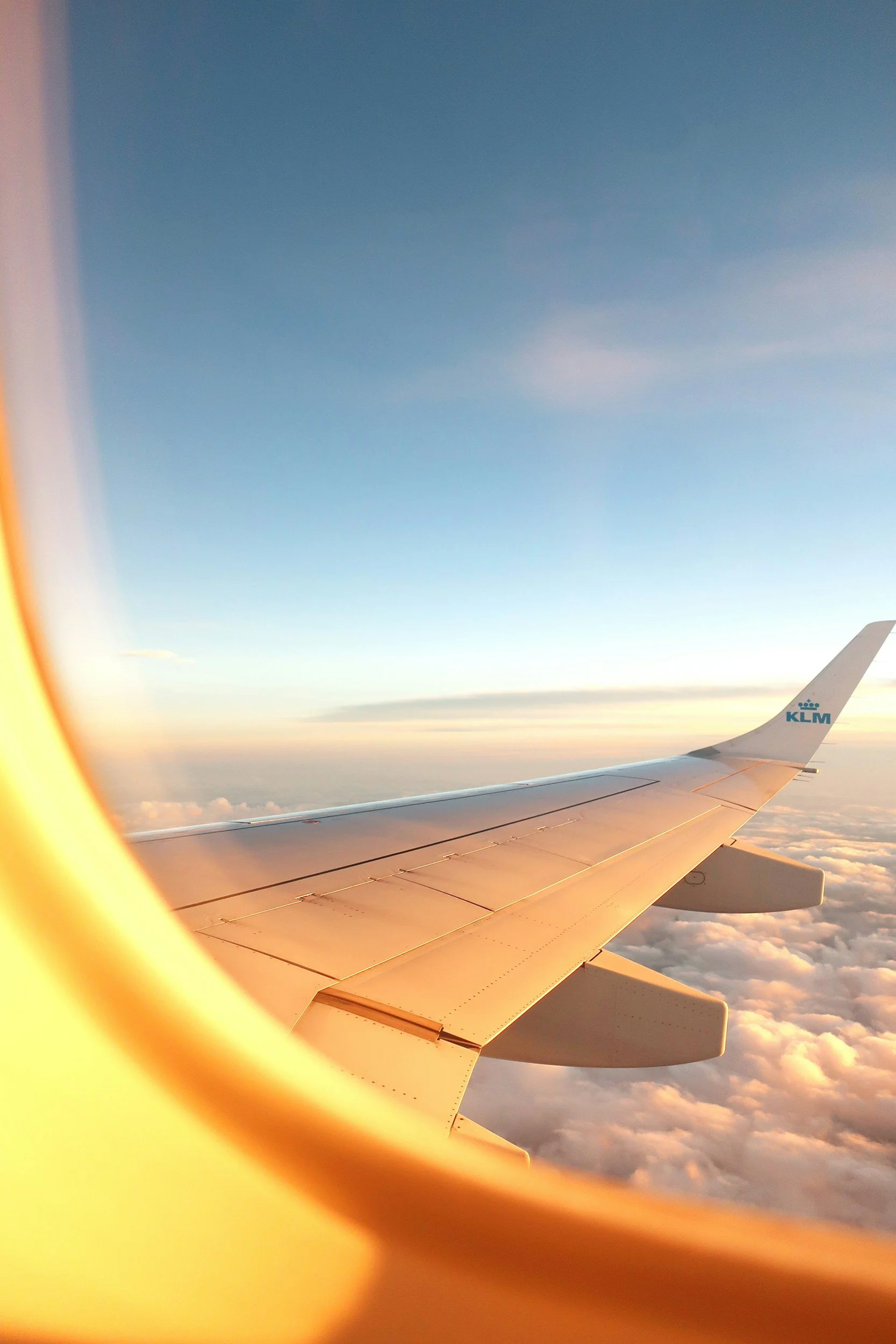 View from airplane window showing wing and clouds during sunset