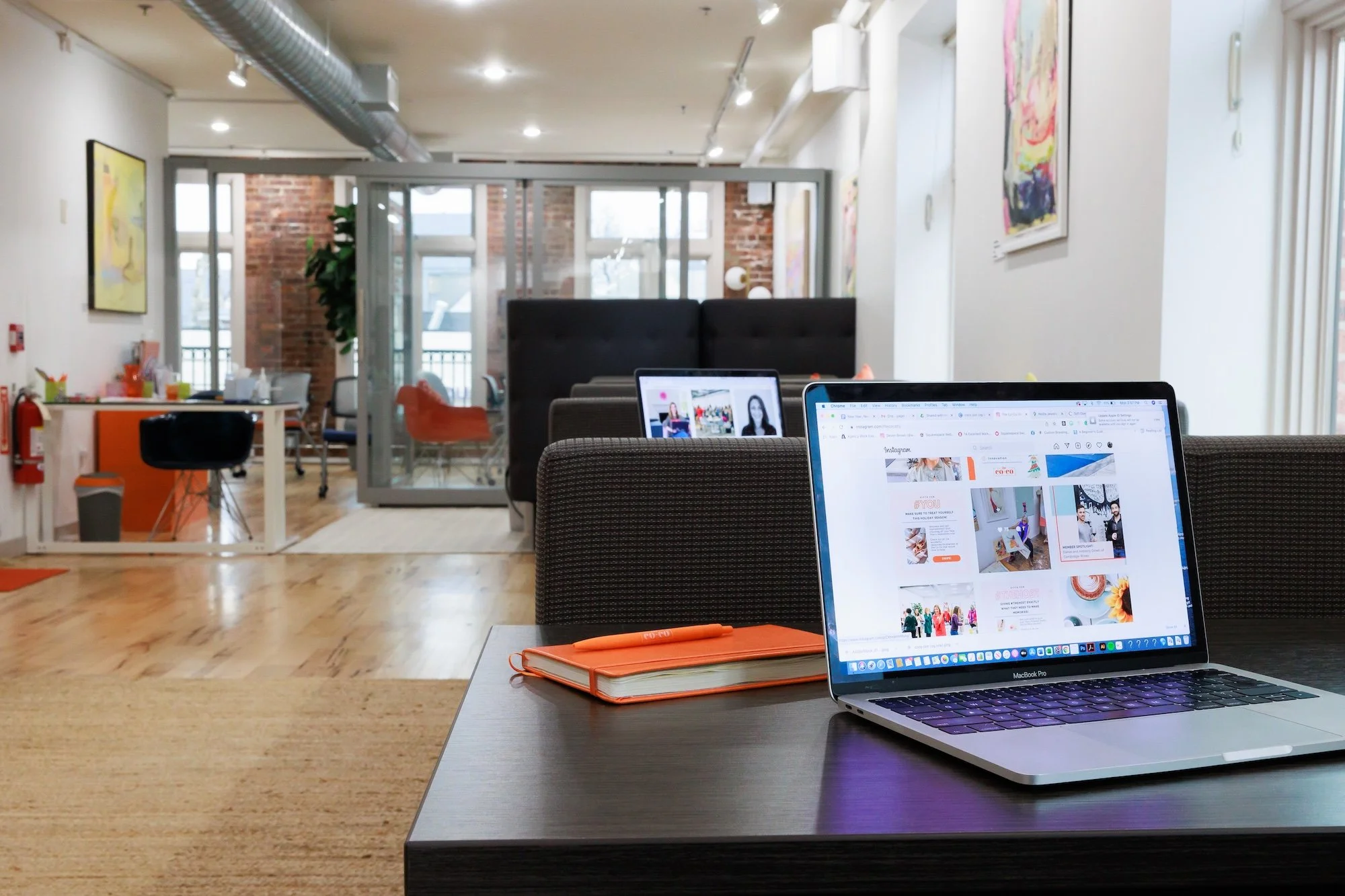 Laptop and orange notebook on a desk in a coworking space