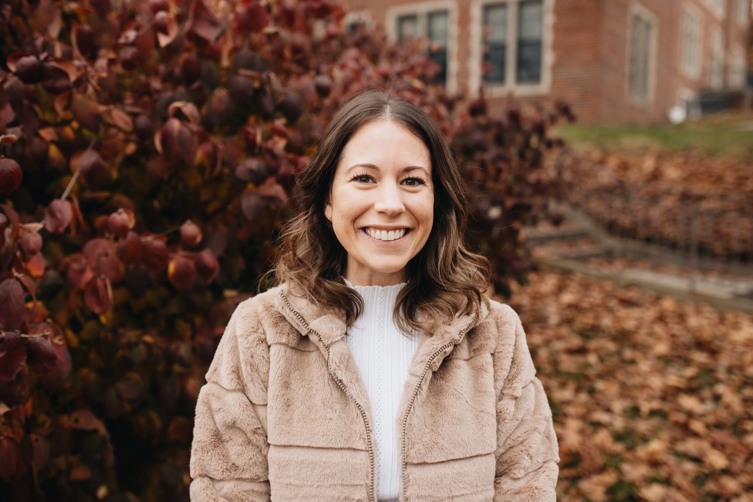 A woman with dark hair wearing a dark green dress with small shiny details, standing on steps in front of a brick building with a wooden arched door and stone trim.